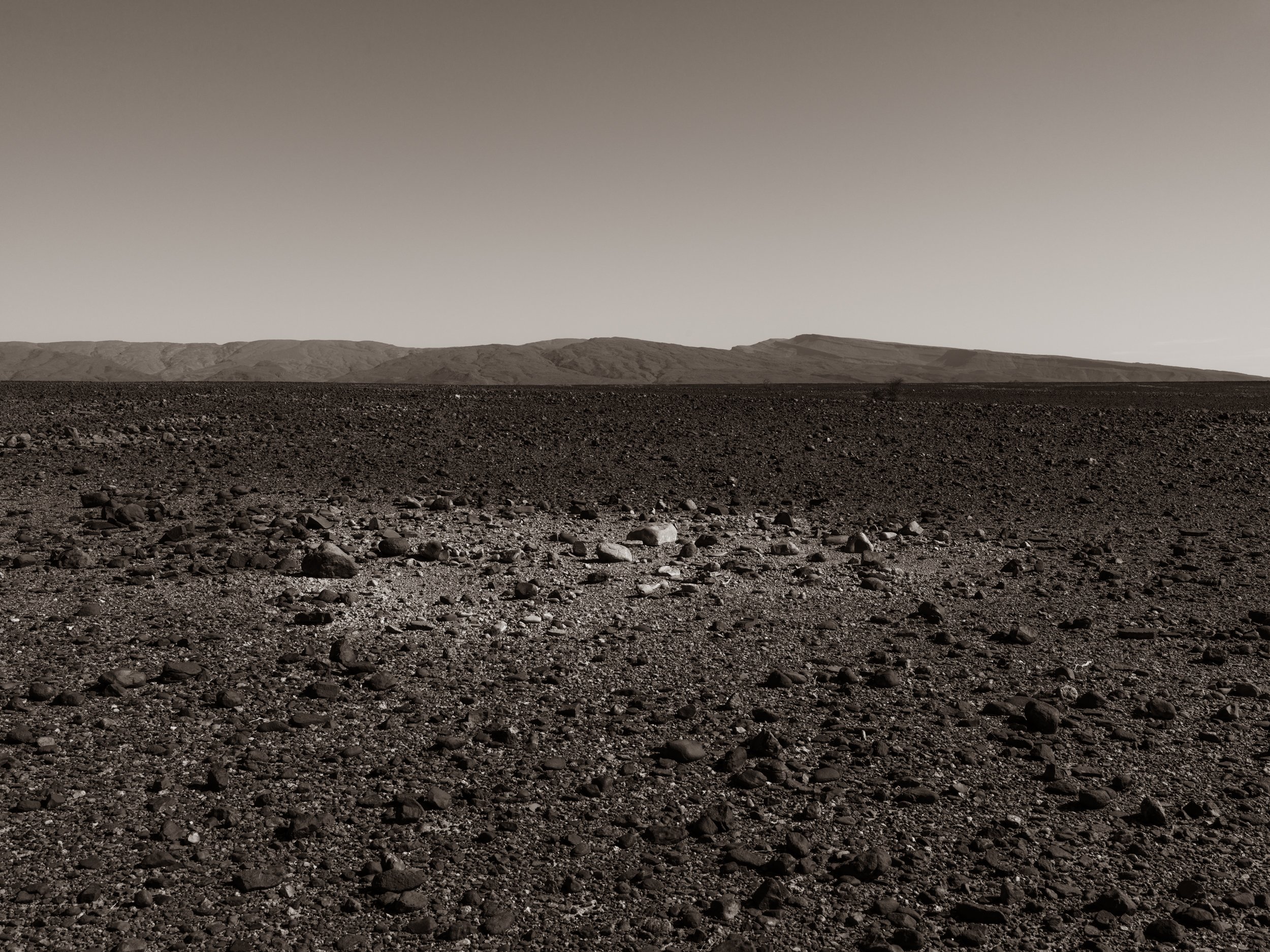 A barren, rocky landscape with distant mountains and a clear sky.