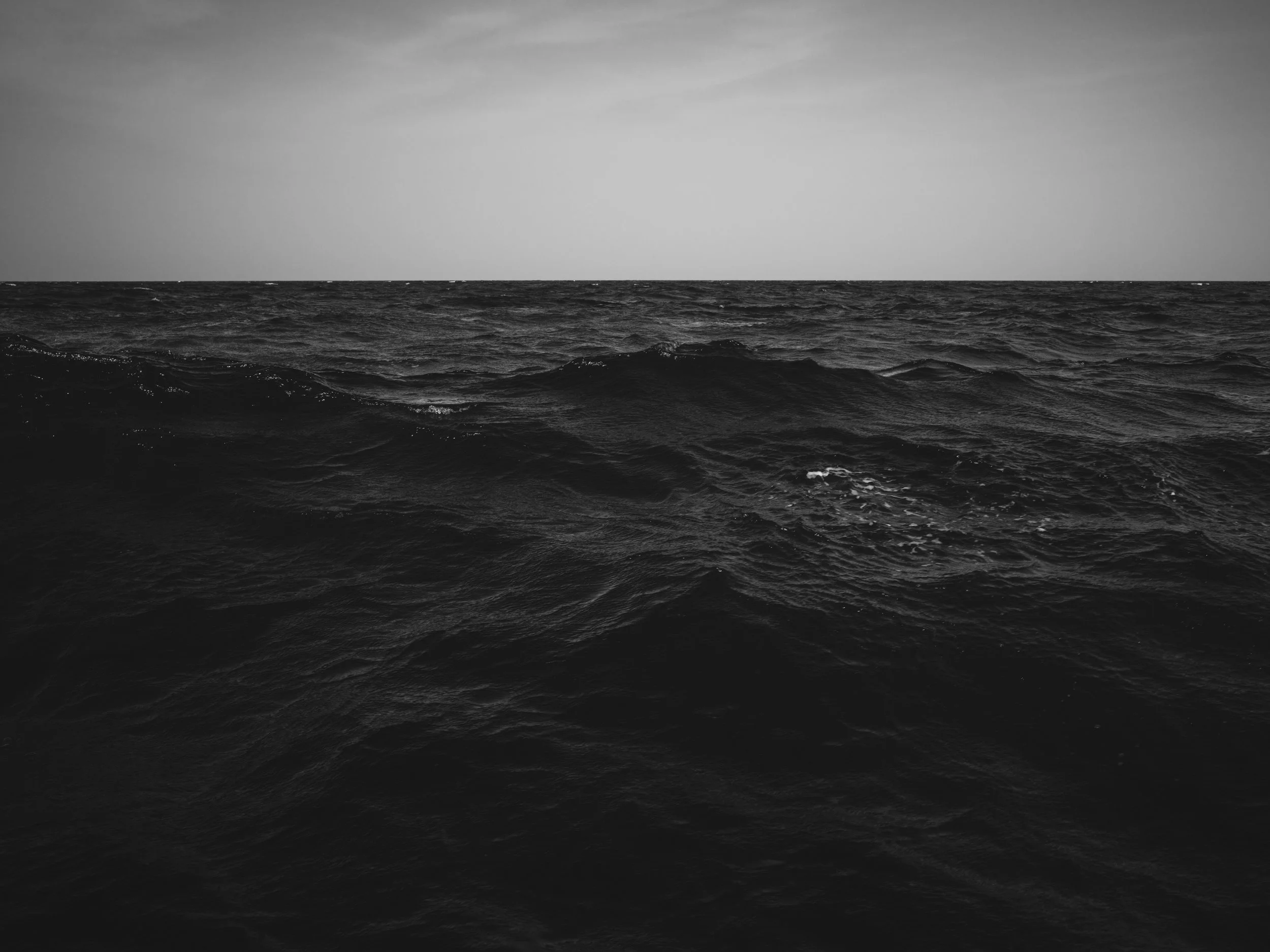 Black and white photo of the ocean with waves and a cloudy sky.