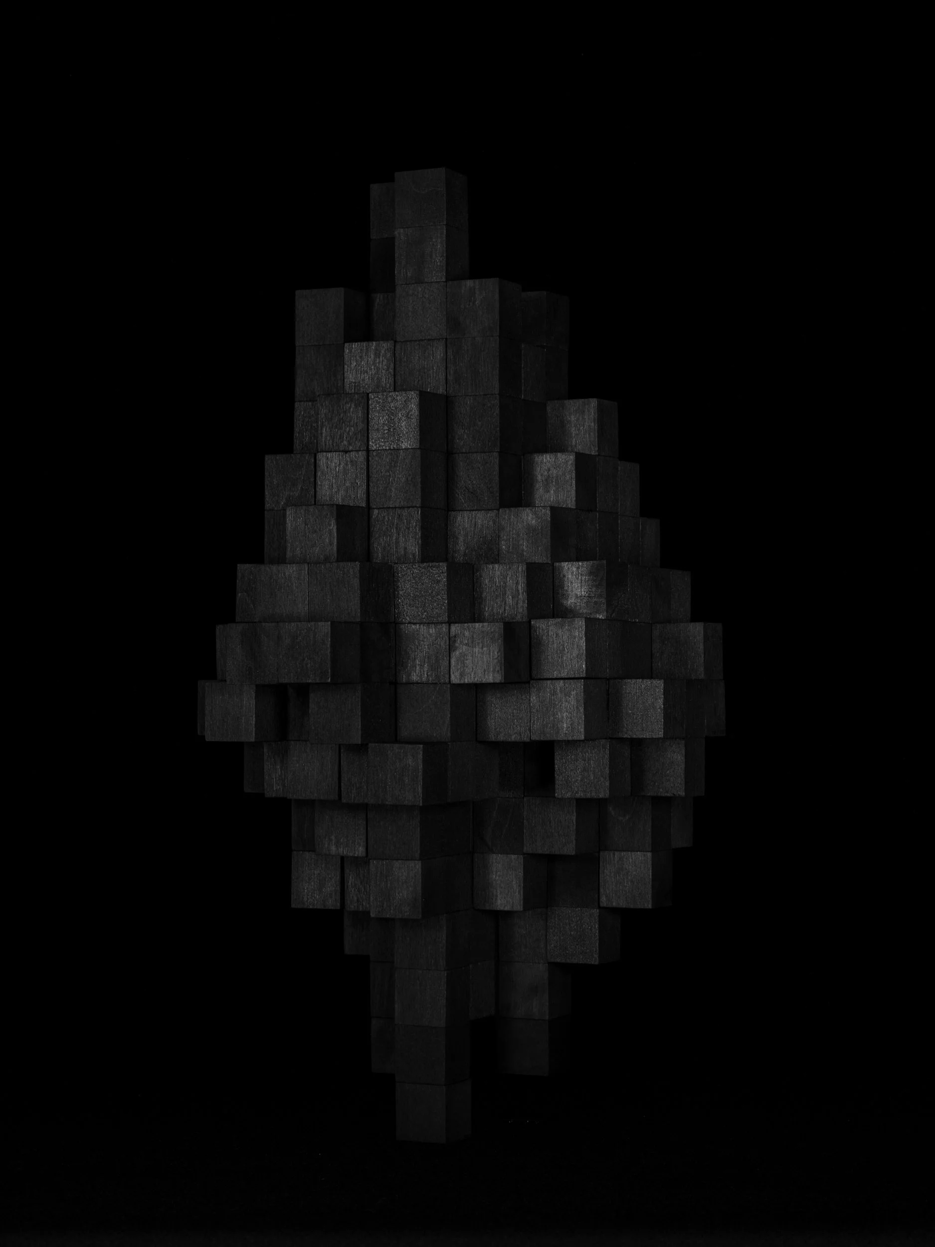 A modern sculpture simulating a pixelated, low resolution image of an asteroid—made of black cubes stacked in an abstract shape against a black background.