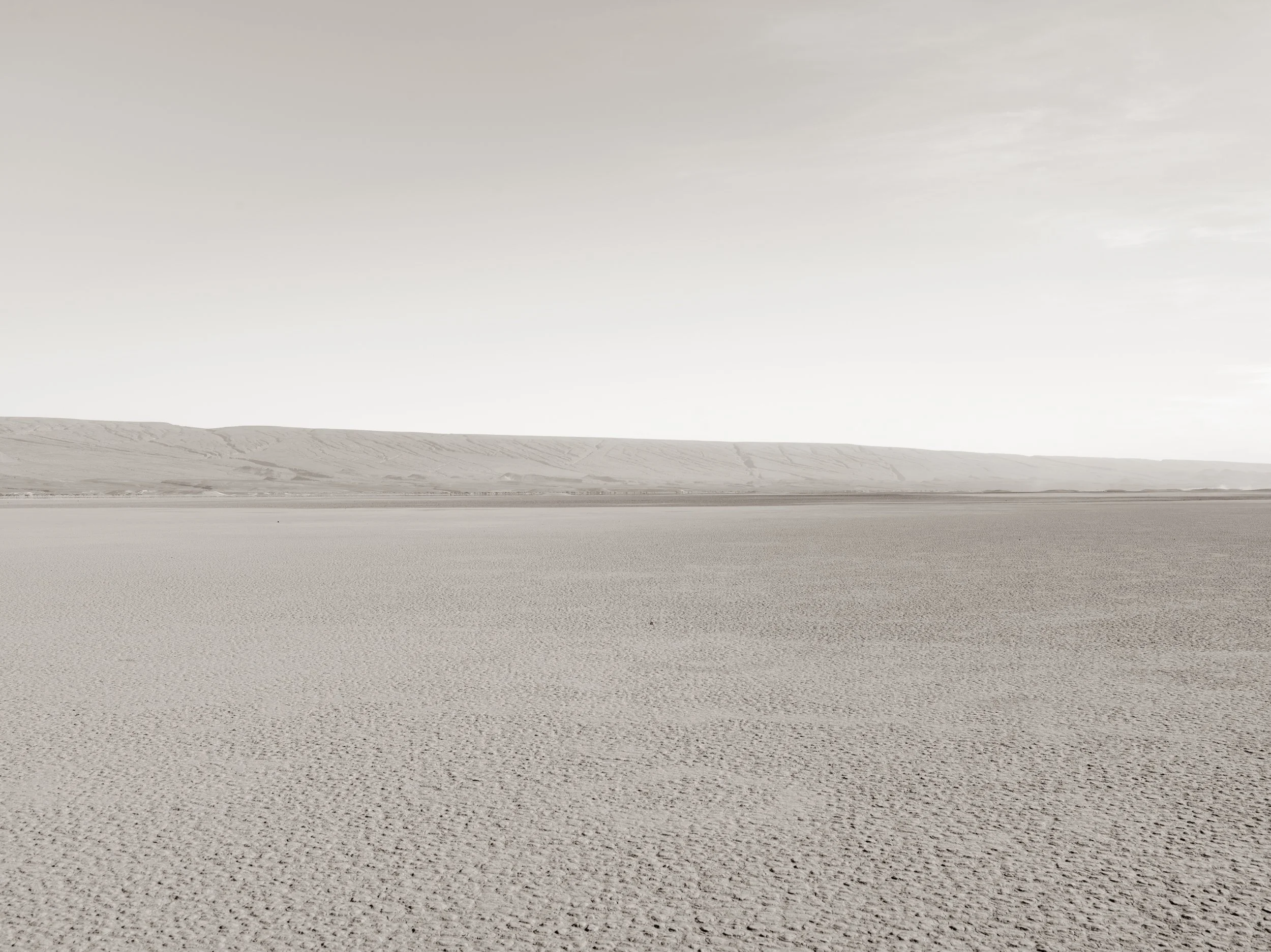 A vast, flat salt flat under a cloudy sky, with distant hills on the horizon.