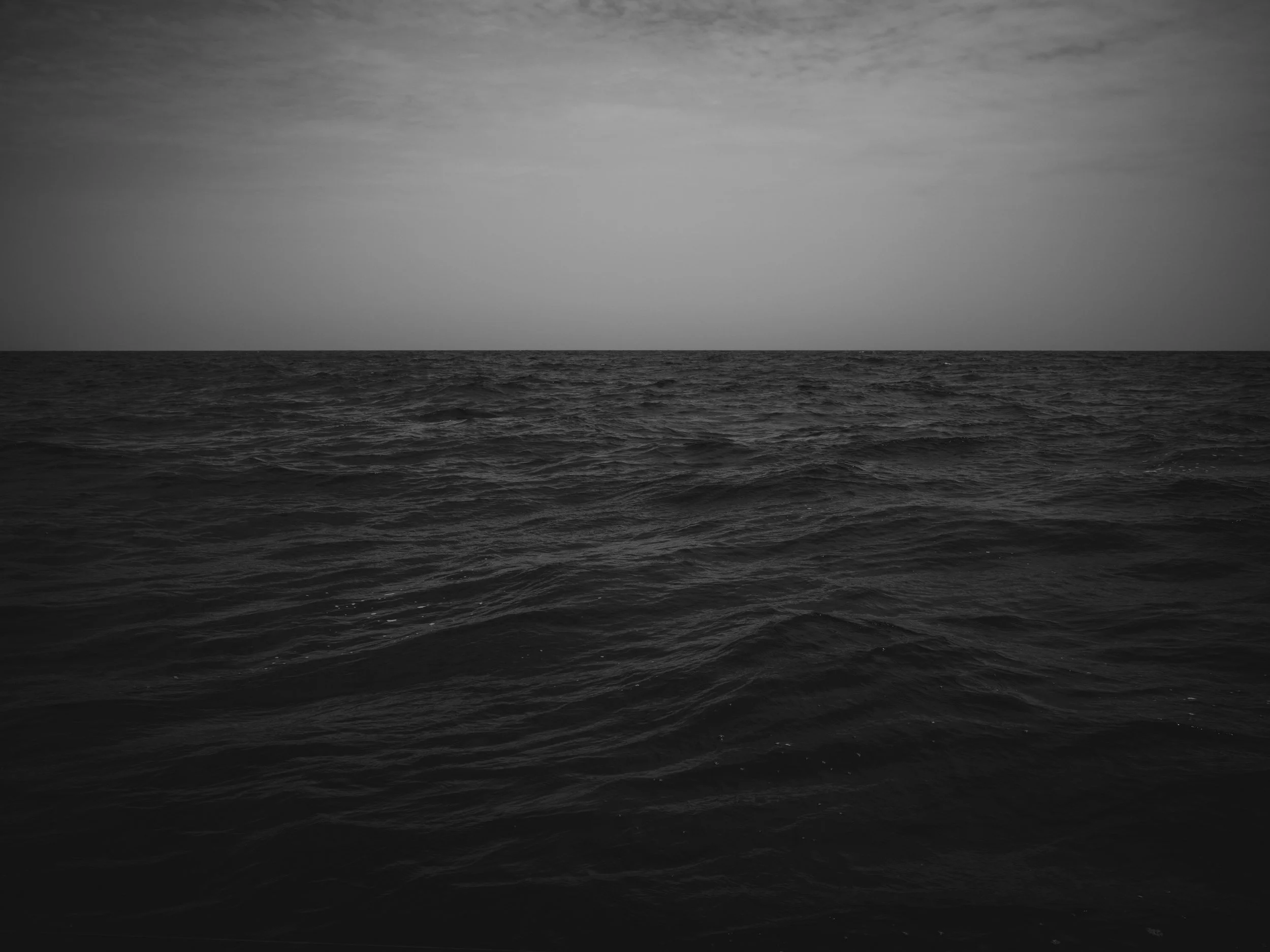 Black and white photo of a vast ocean with a cloudy sky above.