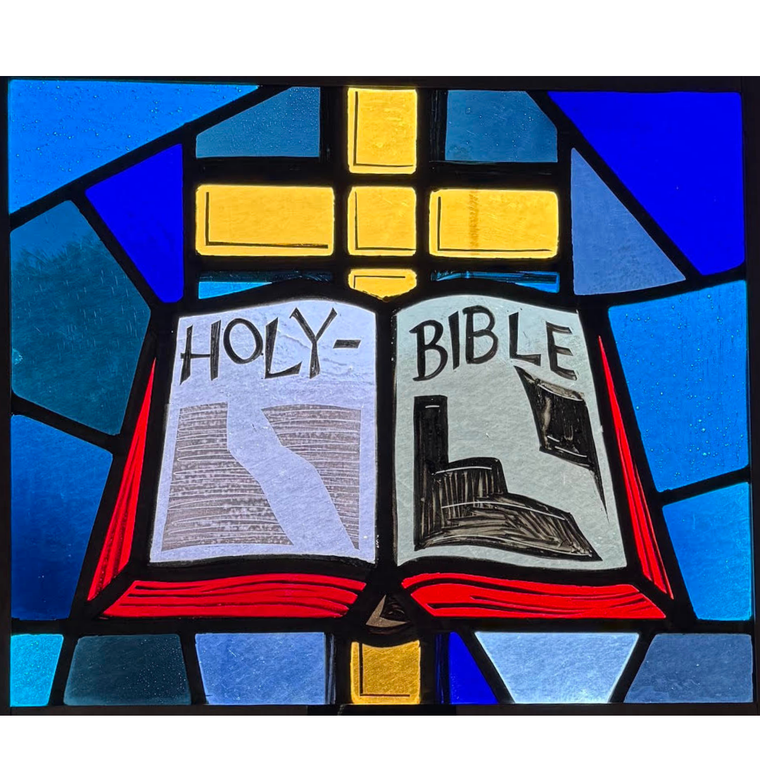 Stained glass window depicting an open Bible with the words 'Holy Bible' and illustrations of the Bible pages.
