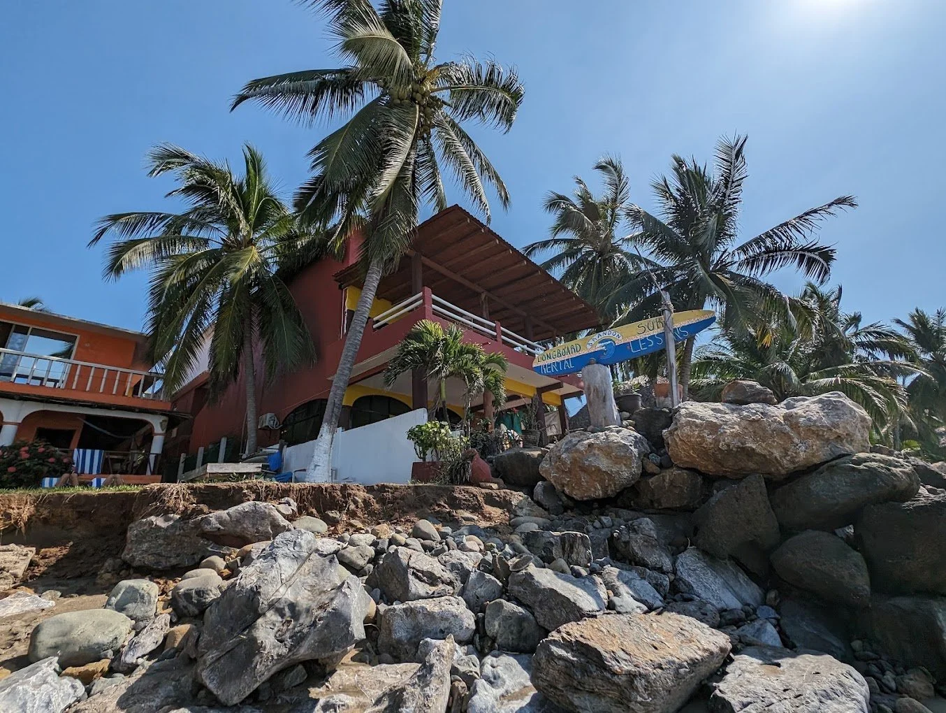 Casa Esmeralda seen from the rocky shoreline beneath palm trees