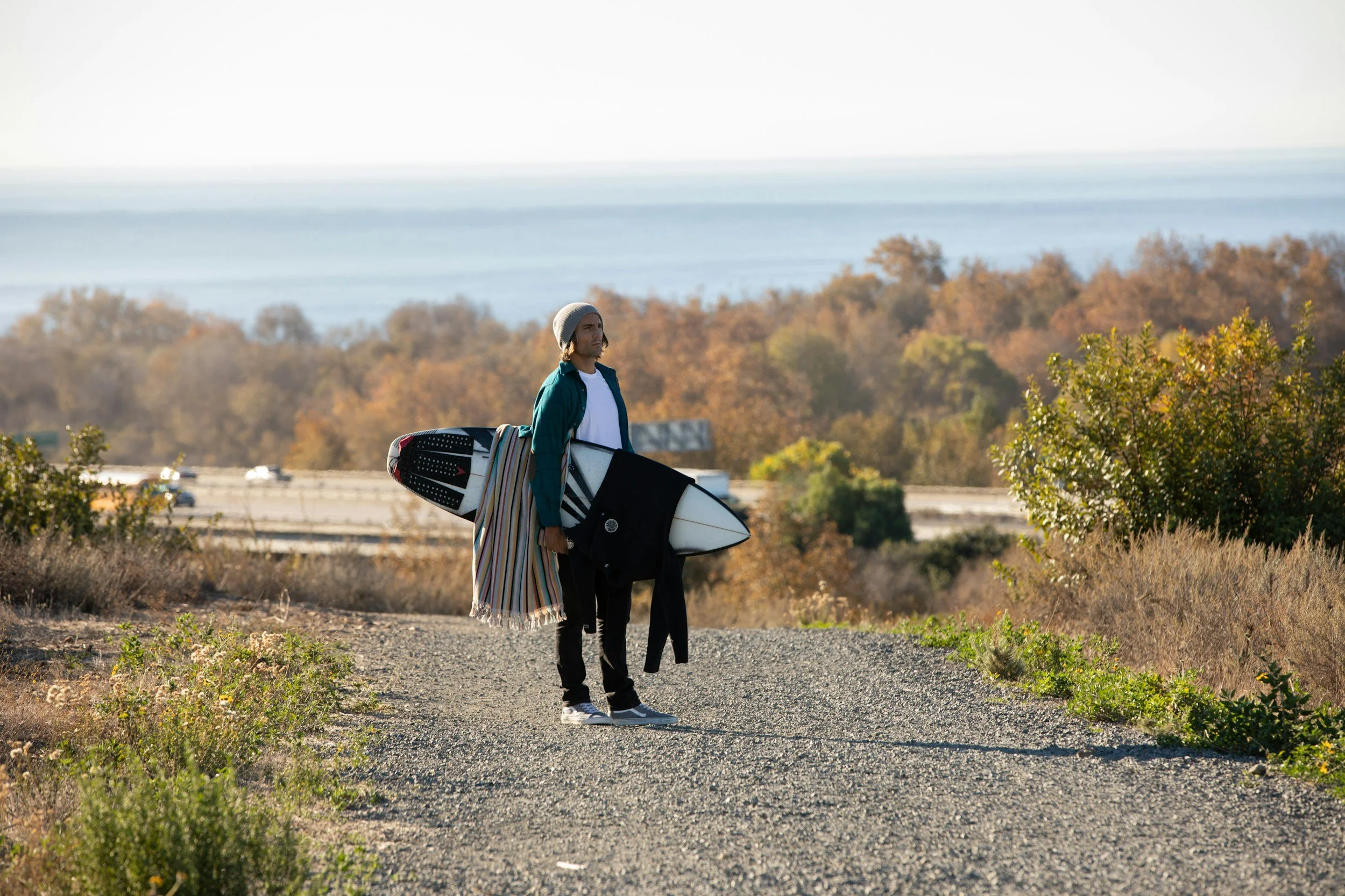 Surfer walking a coastal trail near San Onofre, California, carrying a surfboard toward the ocean
