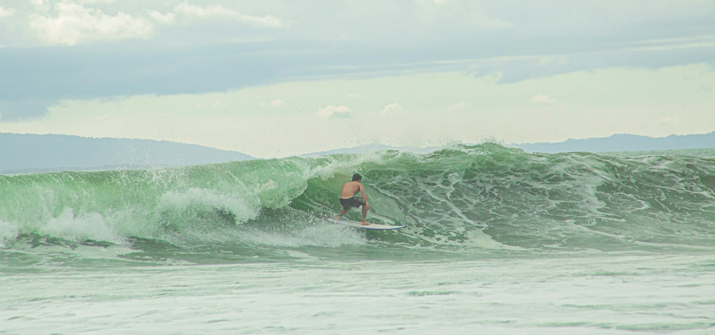 Surfer riding a long, green left-hand wave at Pavones, Costa Rica