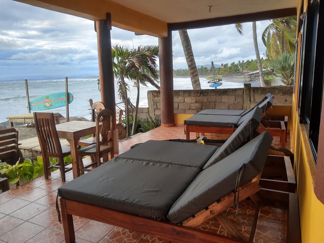 Padded loungers on a covered patio looking out to the beach and ocean