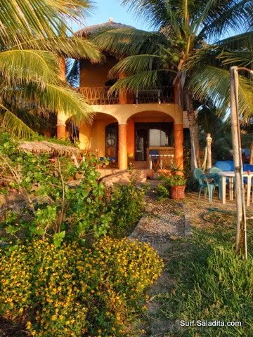 Orange beach house with an arched porch, palm trees and a flowering garden path