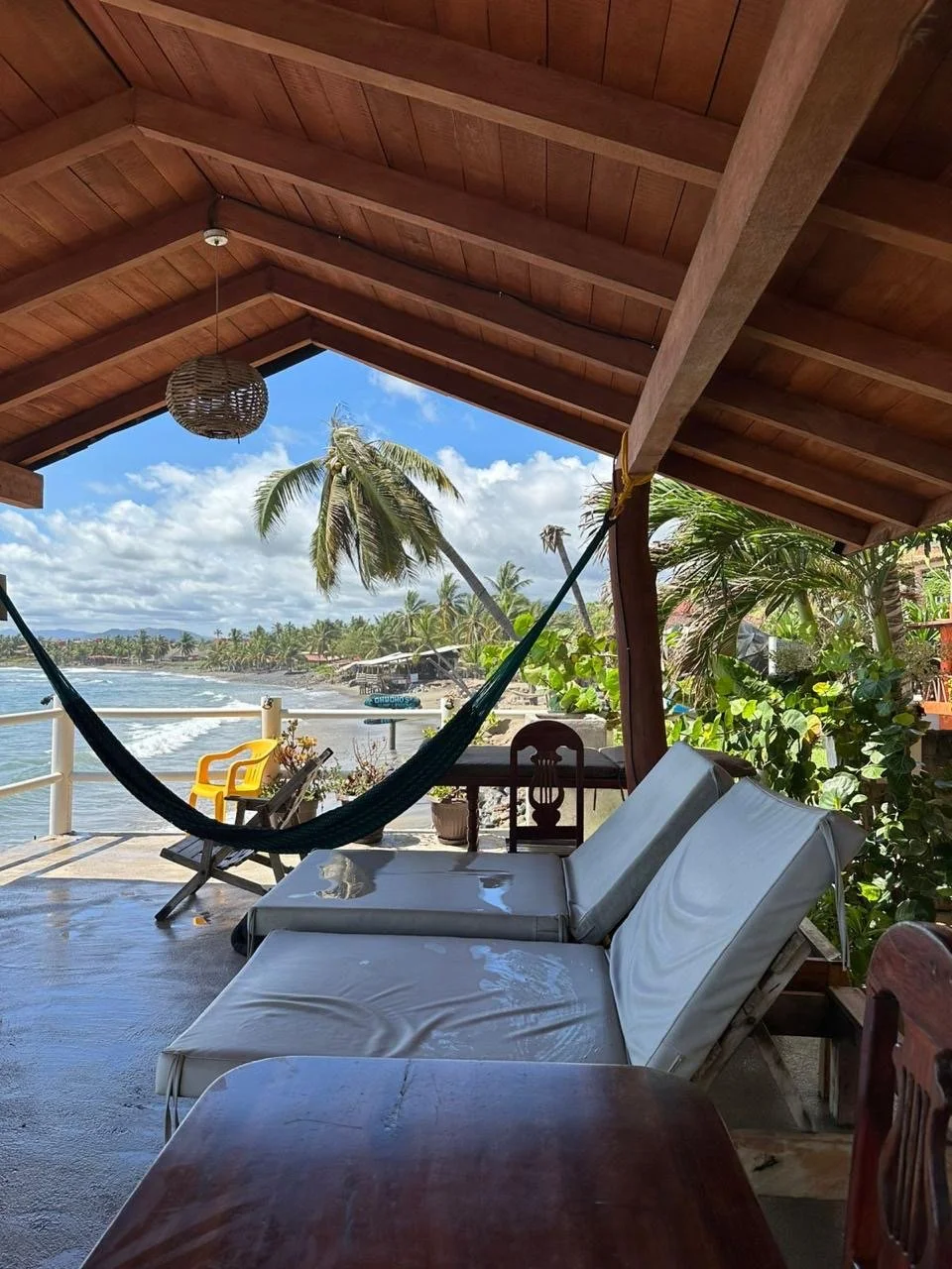 Covered terrace with a hammock and lounge chairs overlooking the beach