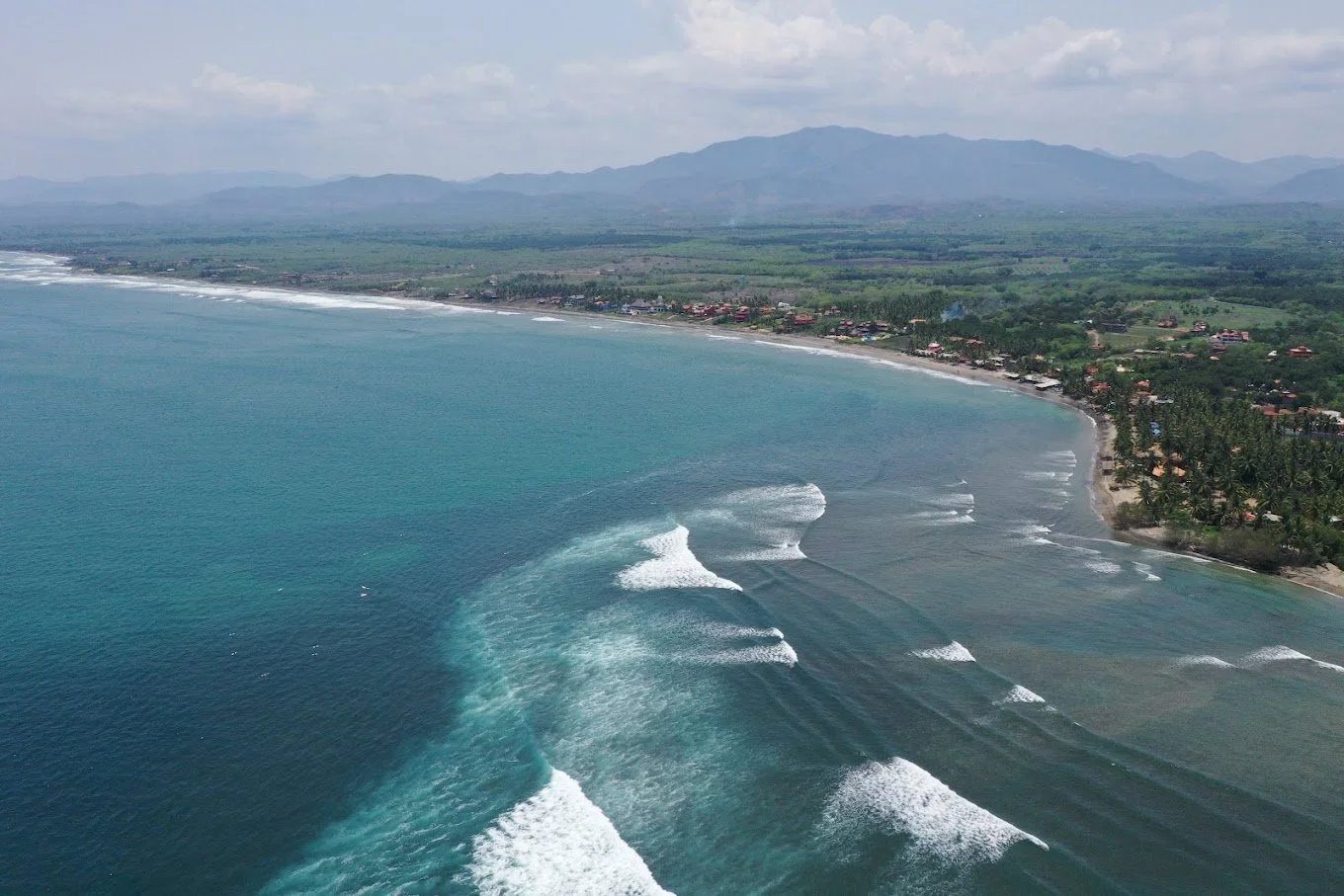Aerial view of waves breaking across La Saladita bay with mountains behind