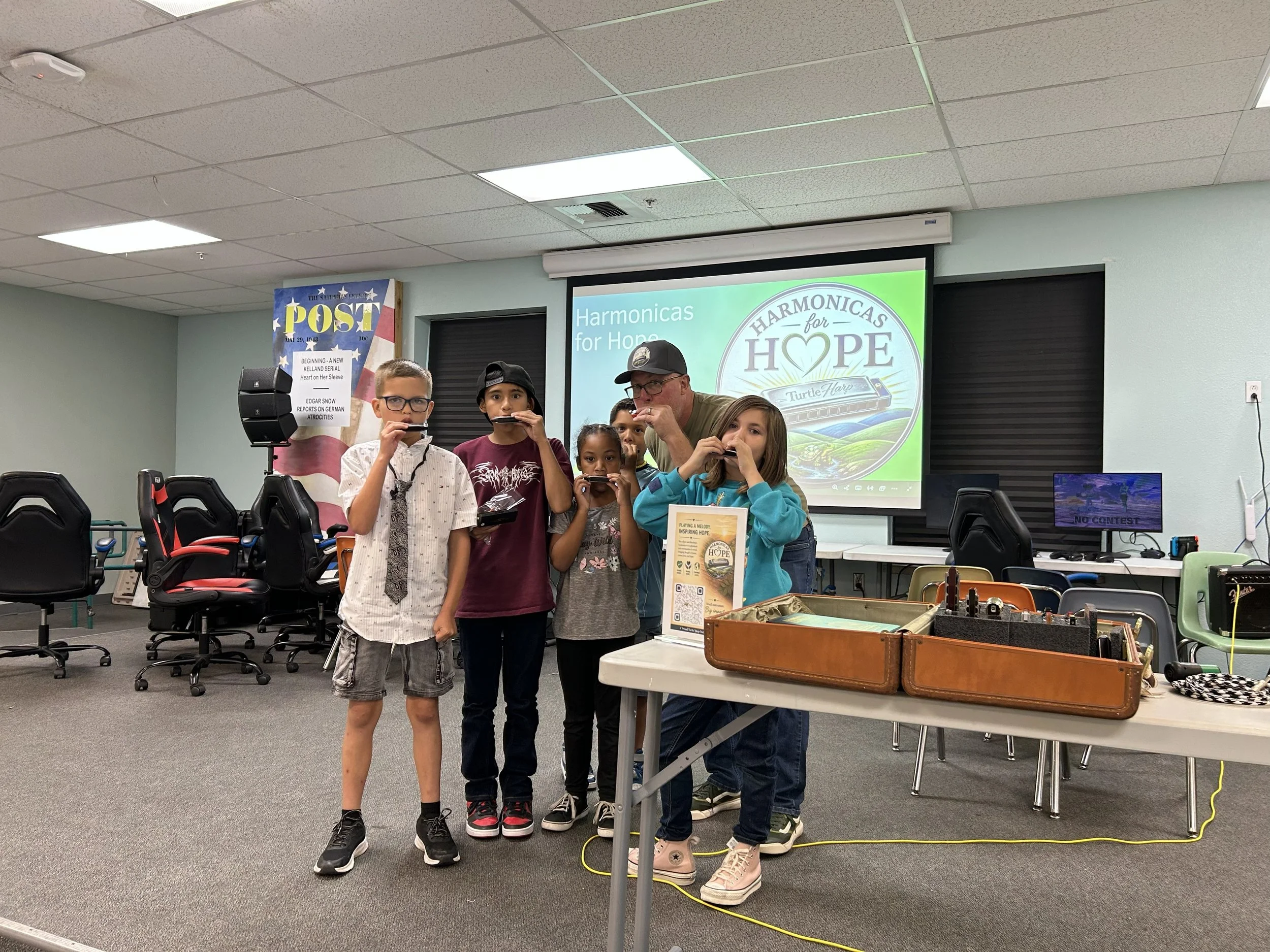 Children and an adult playing harmonicas in a classroom with a projector screen that reads 'Harmonics for Hope'