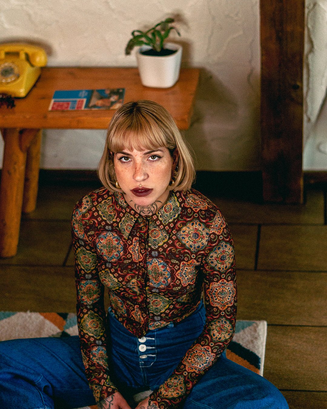 Jeune femme aux cheveux courts, portant une chemise à motifs colorés, assisse sur le sol, vue de dessus.