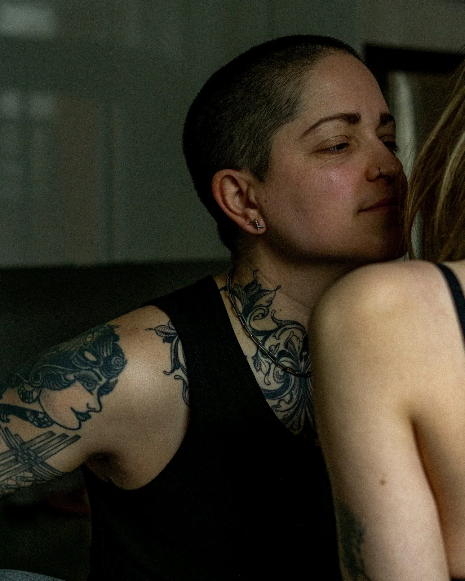 Une femme avec une tête rasée, portant un anneau nasal, des tatouages sur le bras, et portant une chaîne