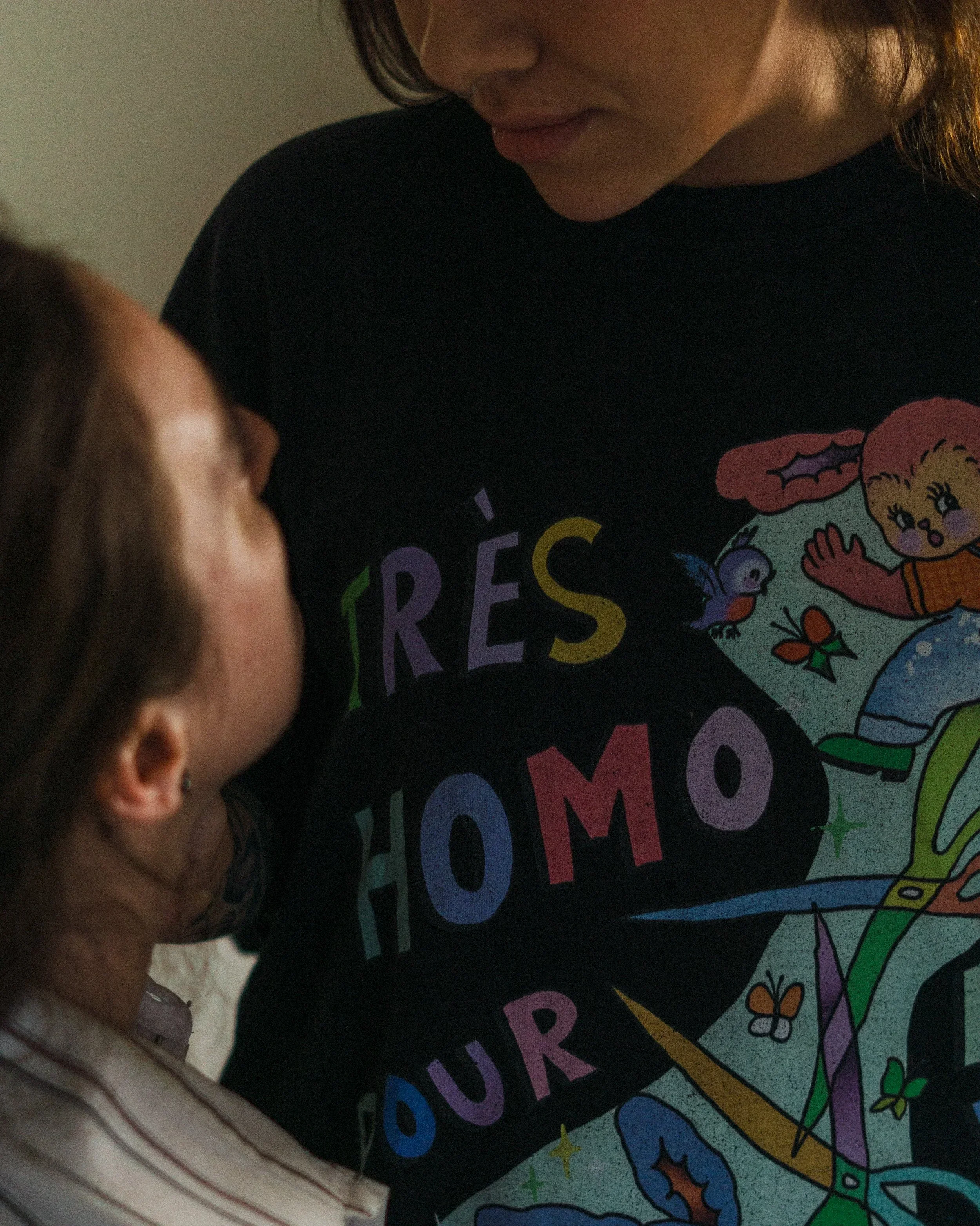 Une fille aux cheveux bruns courts regarde une affiche colorée contenant des dessins, des lettres colorées et des motifs. La fille porte une chemise à rayures.