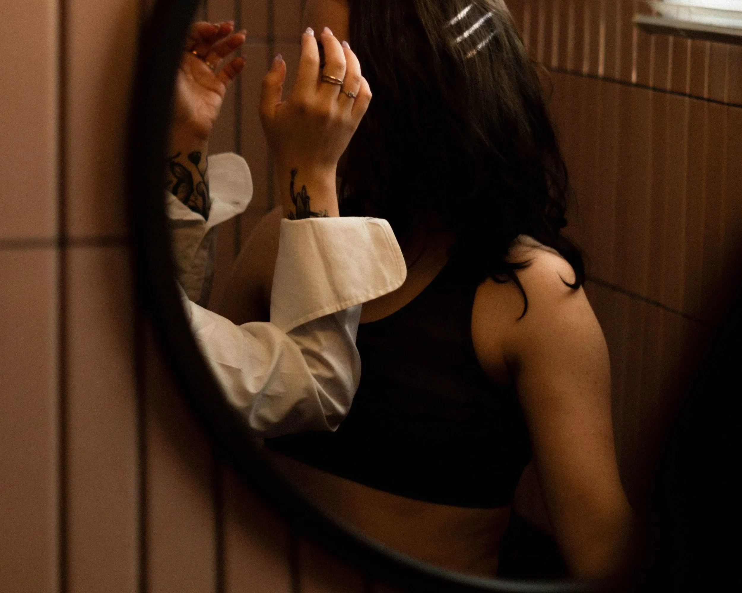 Une personne avec des tatouages sur les bras, portant une bague, semble être en souci, et une autre personne est assise à côté avec une main près du visage, dans une ambiance sombre et intime.