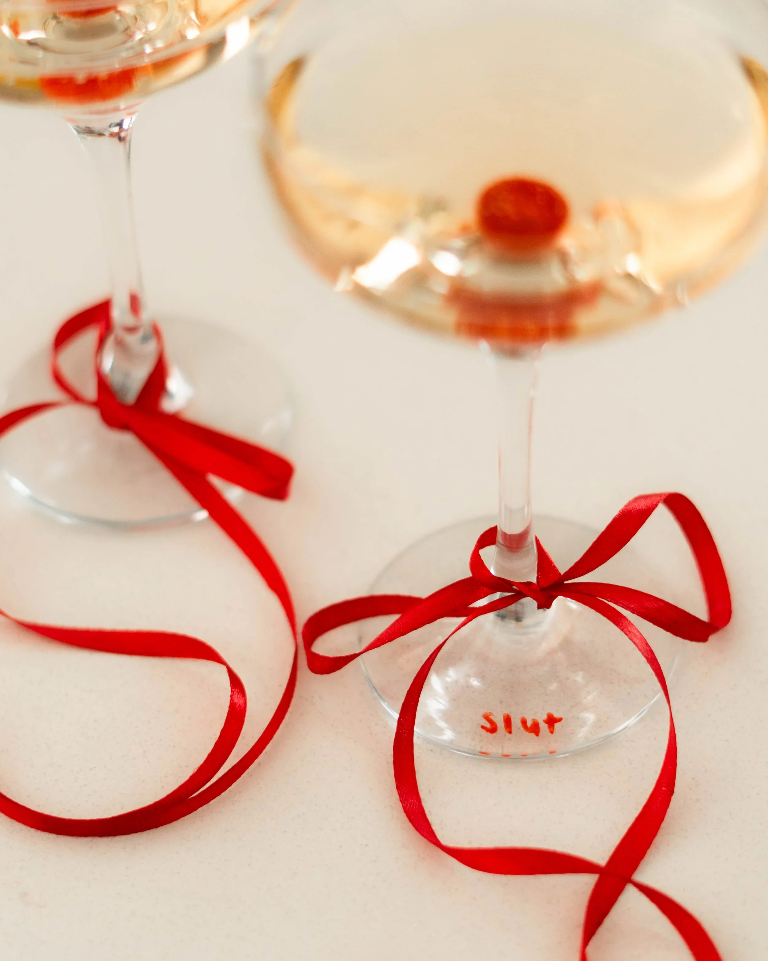 Deux verres de champagne avec des rubans rouges autour, un verre porte une cerise. La vue est floue.
