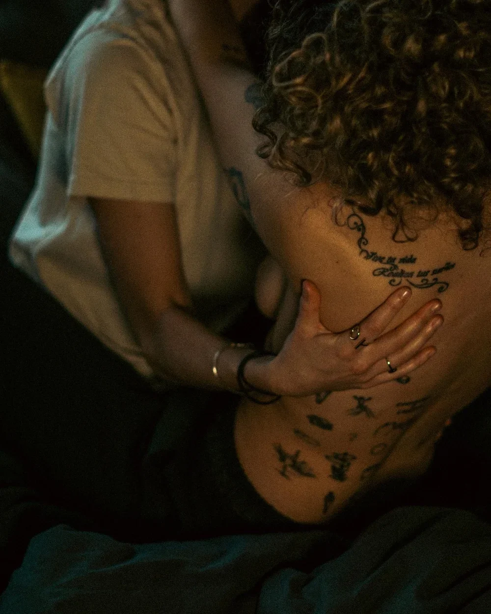 Une personne à moitié nue avec des tatouages sur le dos, tenant la poitrine d'une autre personne.