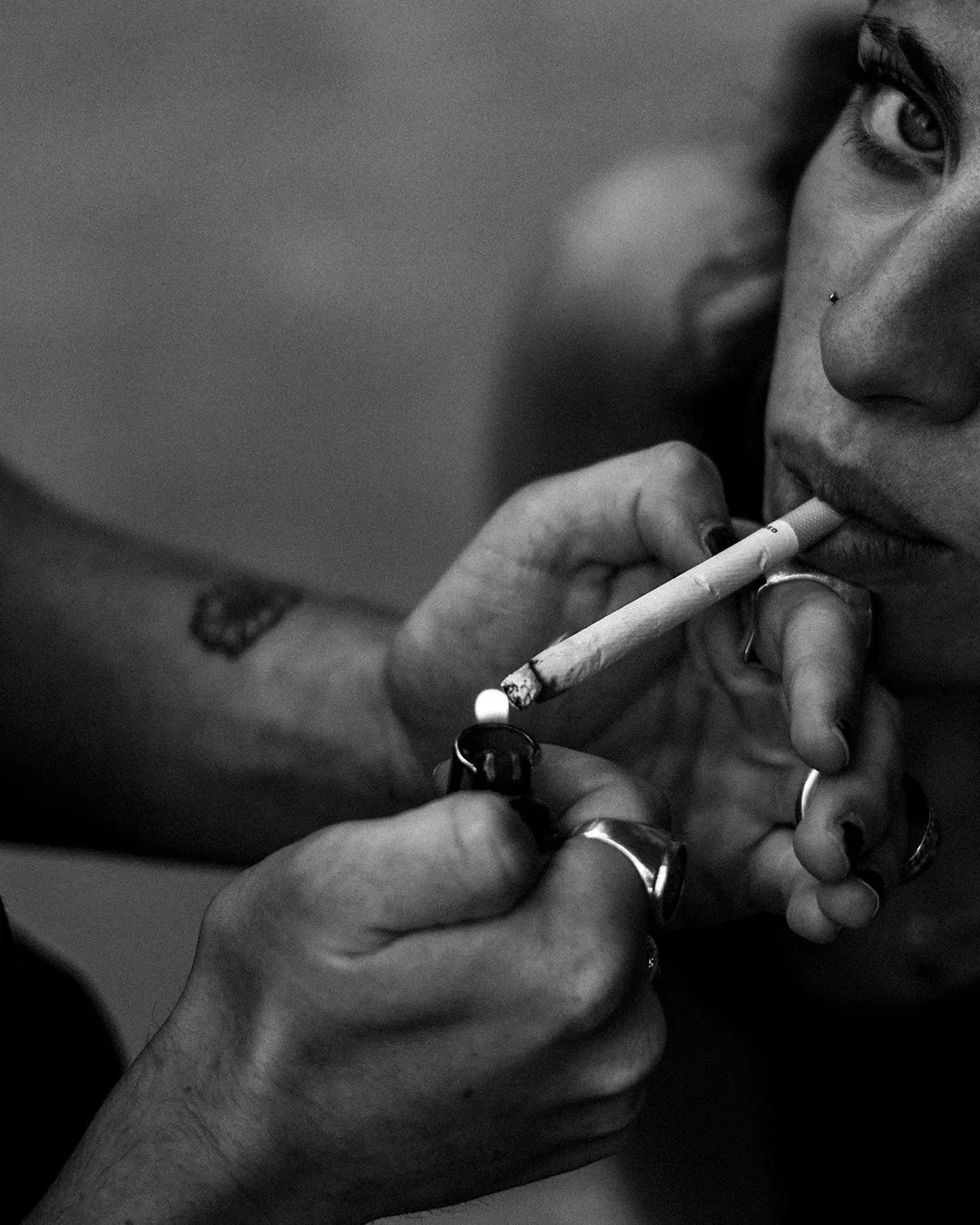 Un gros plan d'une personne qui fume une cigarette, avec un visage partiellement visible, en noir et blanc.