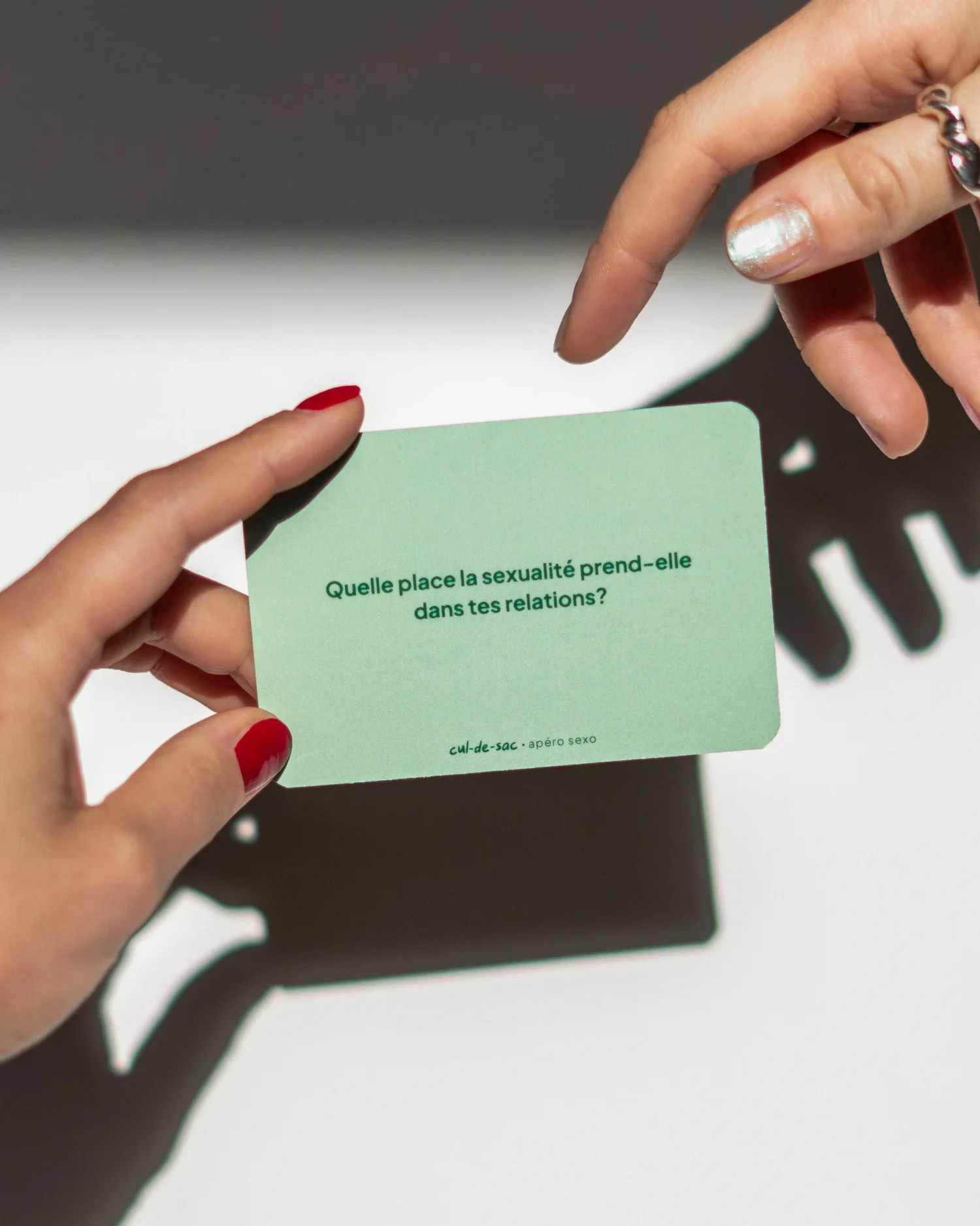 Une main tient une carte verte avec du texte en français qui demande : 'Quelle place la sexualité prend-elle dans tes relations ?'