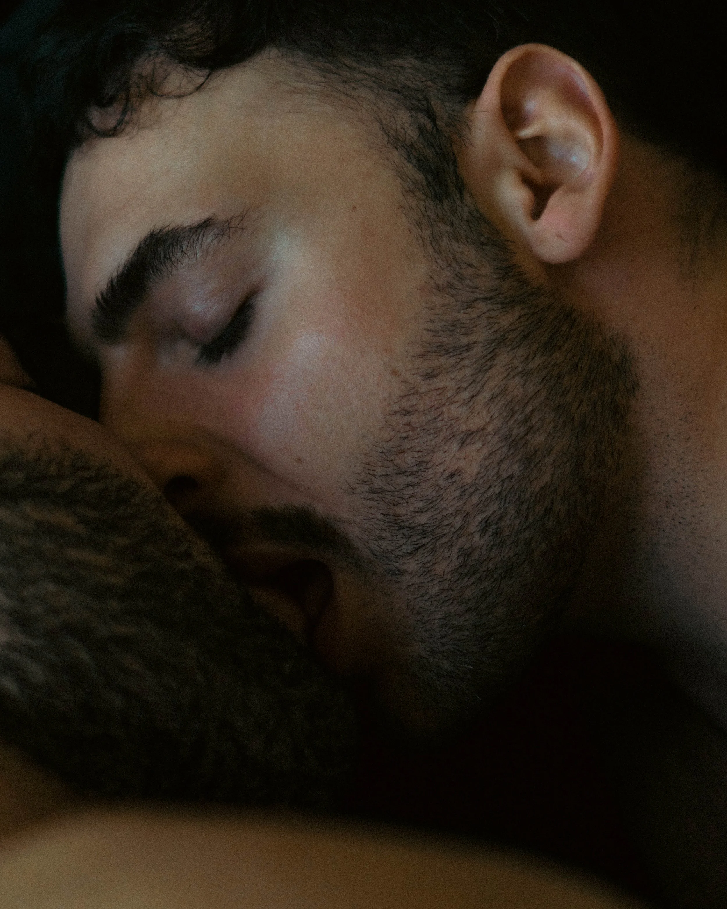 Un visage de jeune homme avec les yeux fermés, des cils longs, des sourcils épais, une barbe de barbe naissante et une peau claire