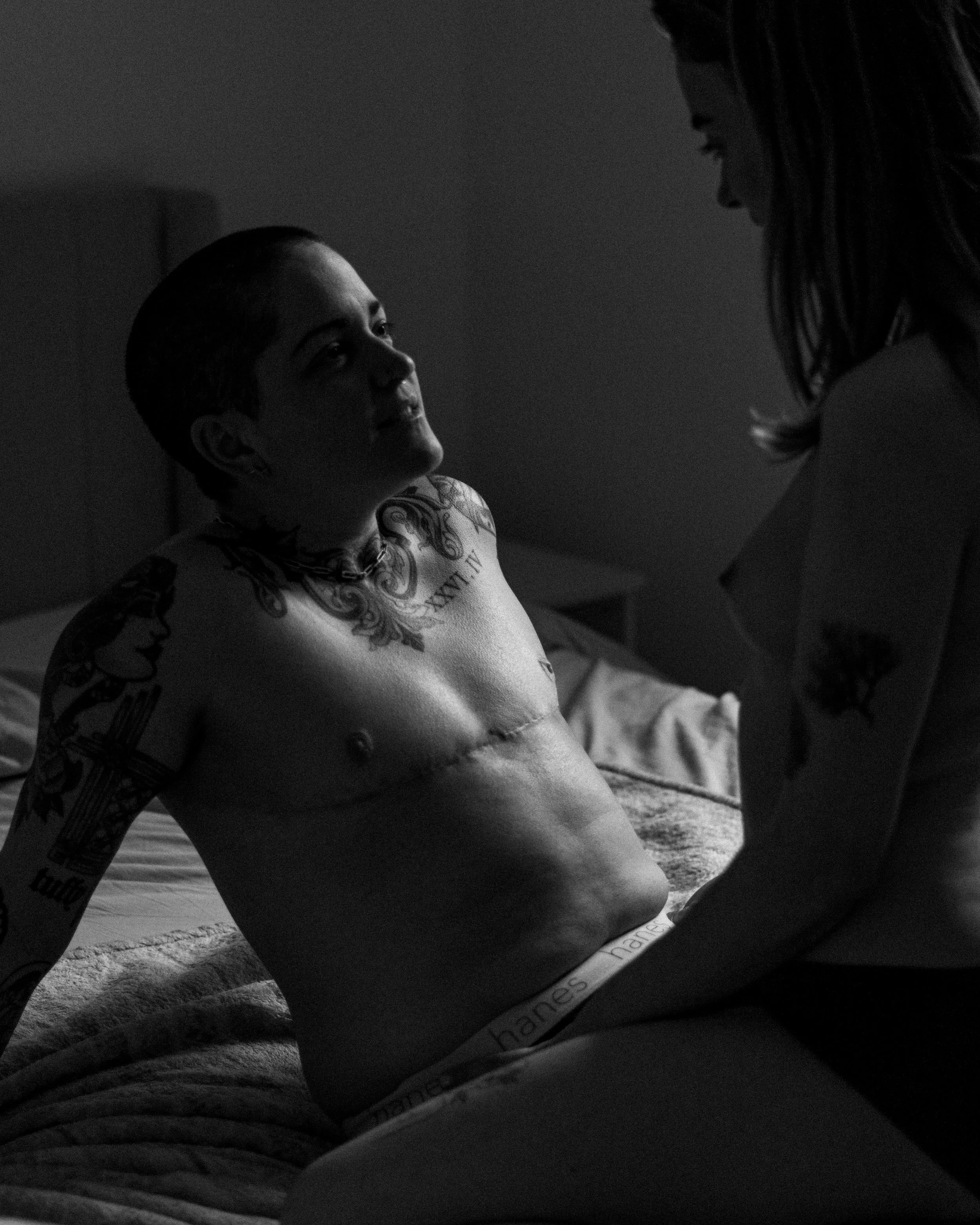 Une femme tatouée se trouve dans un lit, face à un enfant. La scène est en noir et blanc.