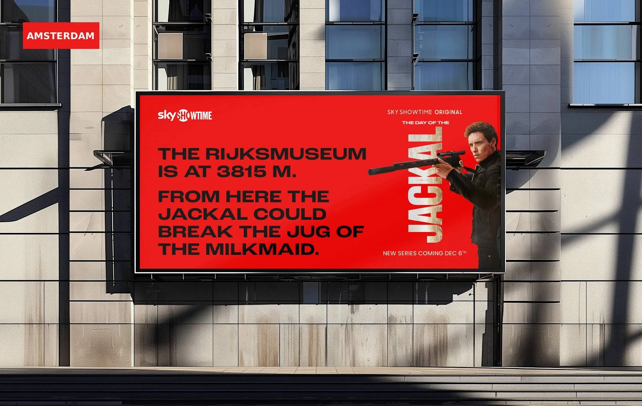 Publicidad exterior en un edificio moderno en Ámsterdam, con un cartel rojo que promociona una serie de televisión, mostrando un hombre con una escopeta y texto en inglés que informa la ubicación y fecha de estreno de la serie.