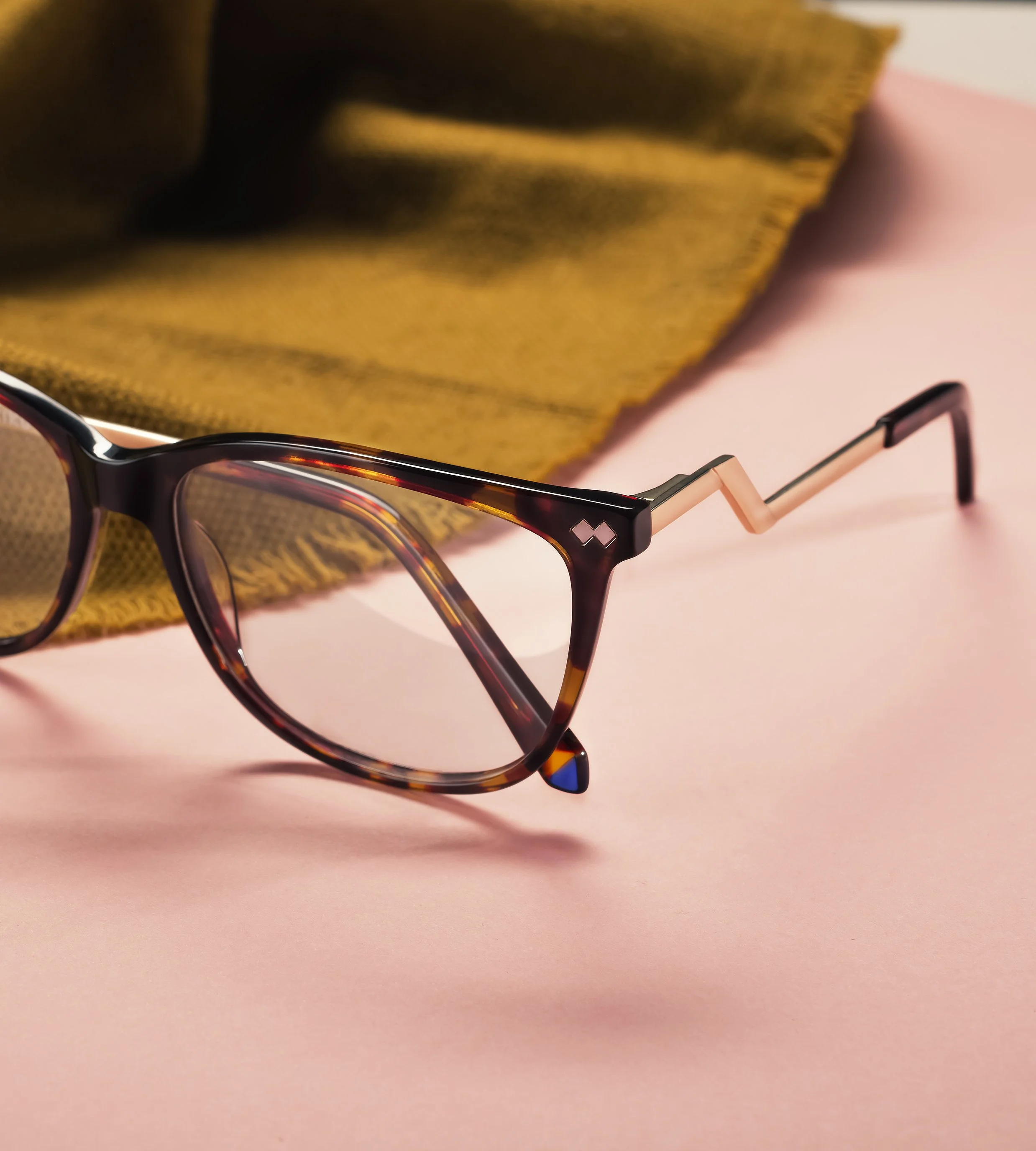 Gafas de sol con marco marrón y detalles en negro, colocadas sobre una superficie rosa