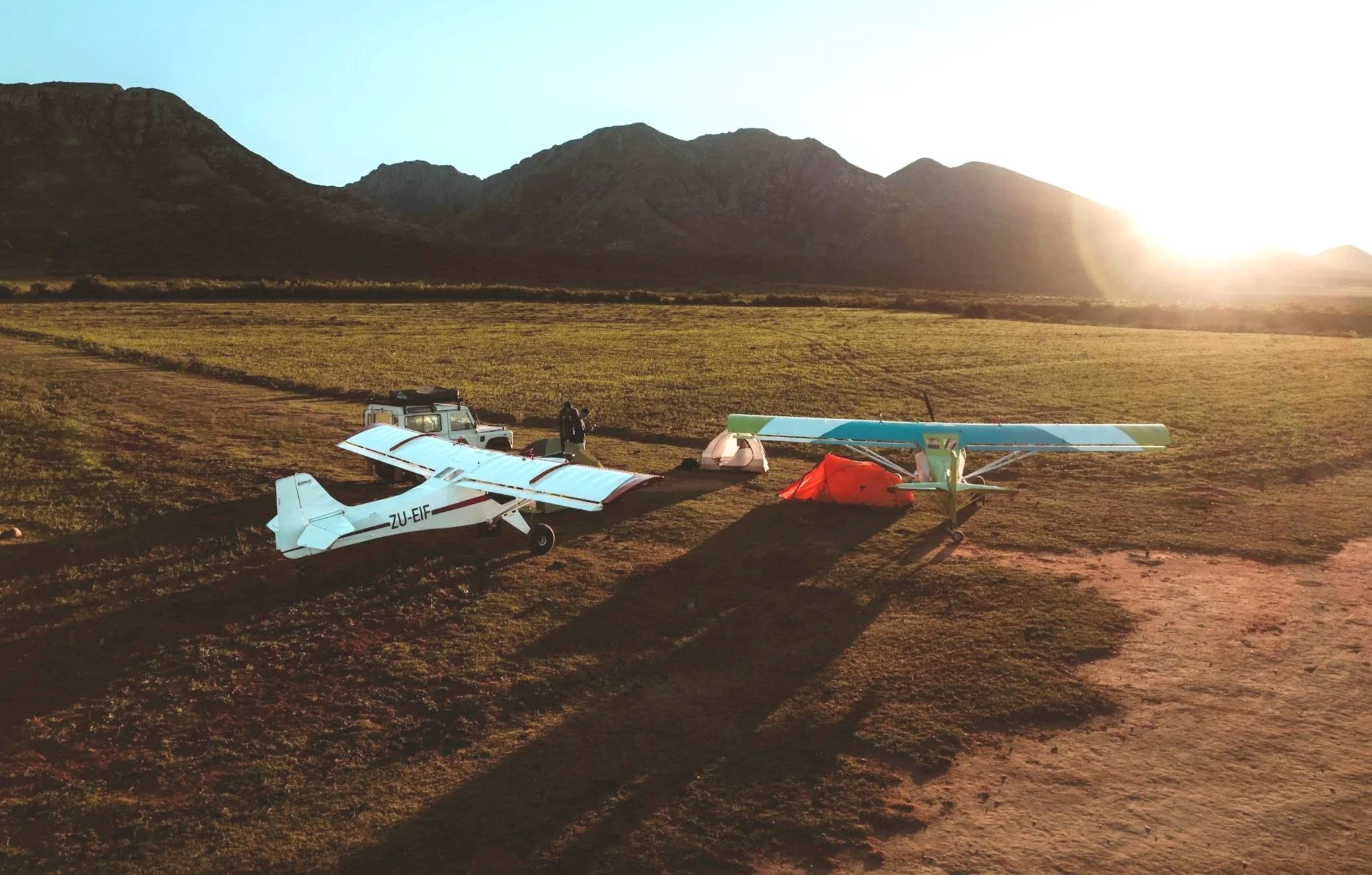Two airplanes in a field with mountains in the horizon