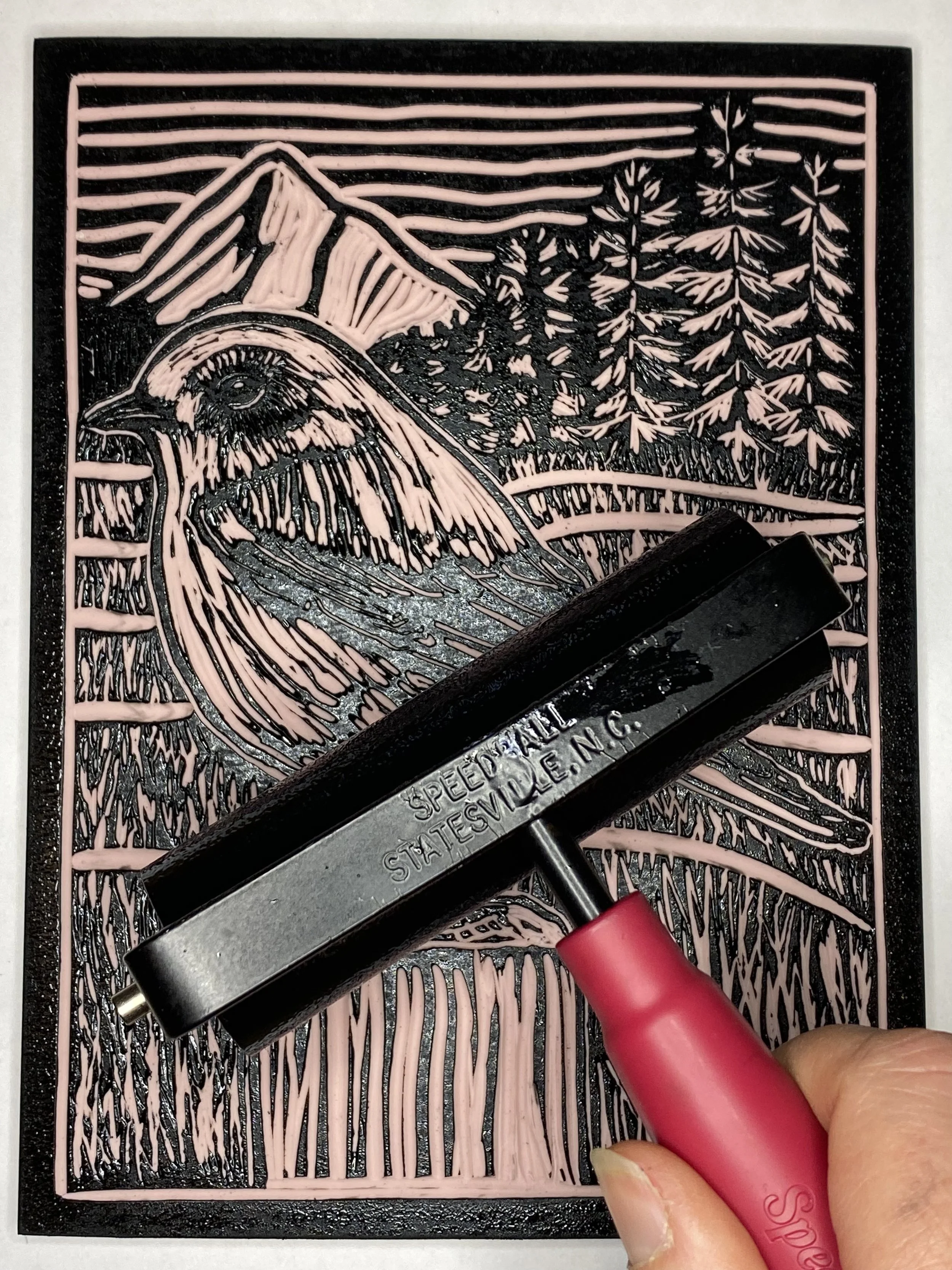 A person using a heat gun to emboss a detailed image of a mountain and trees on a rubber stamp or printing plate.