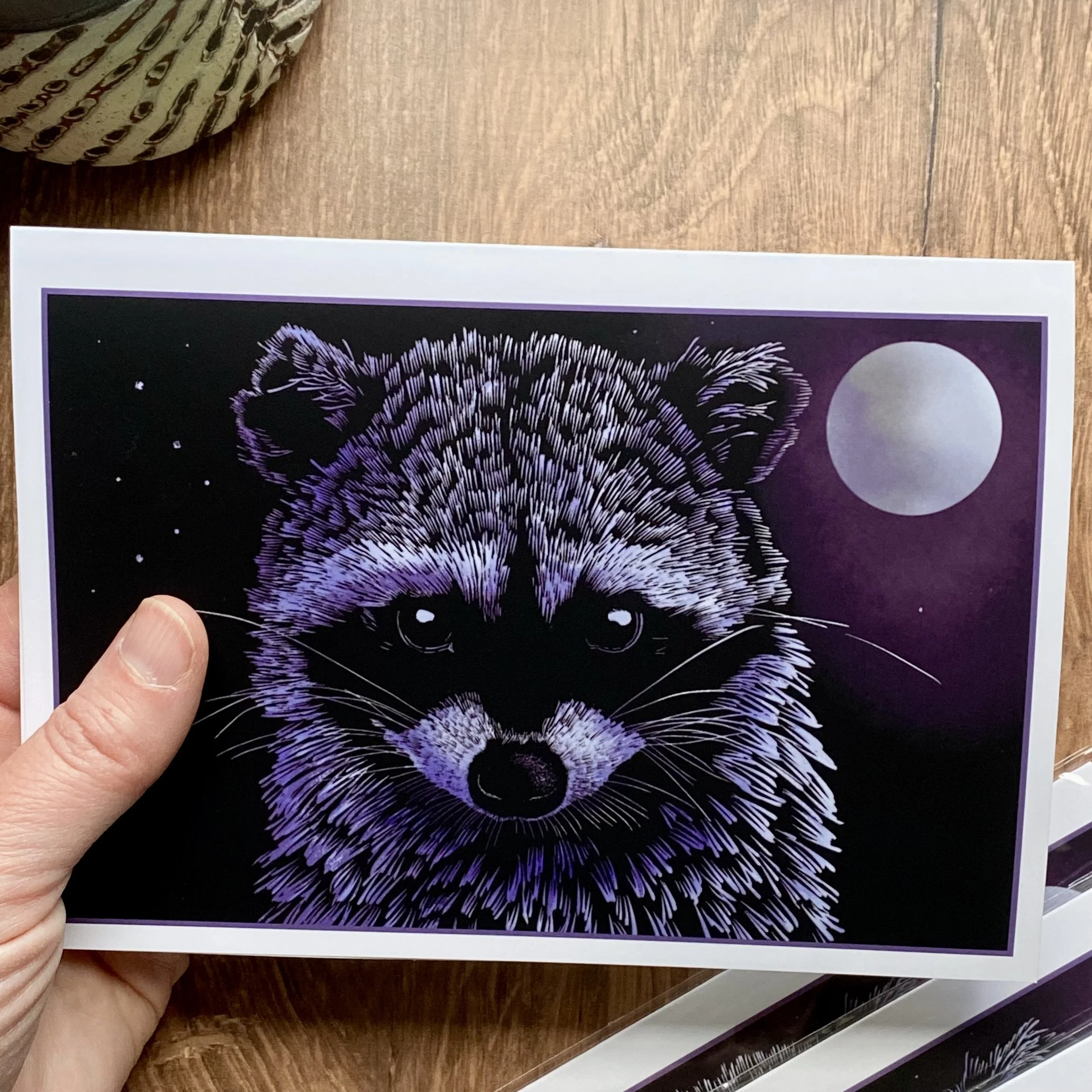 A person holding a black and purple artwork of a bobcat with a moon in the background.