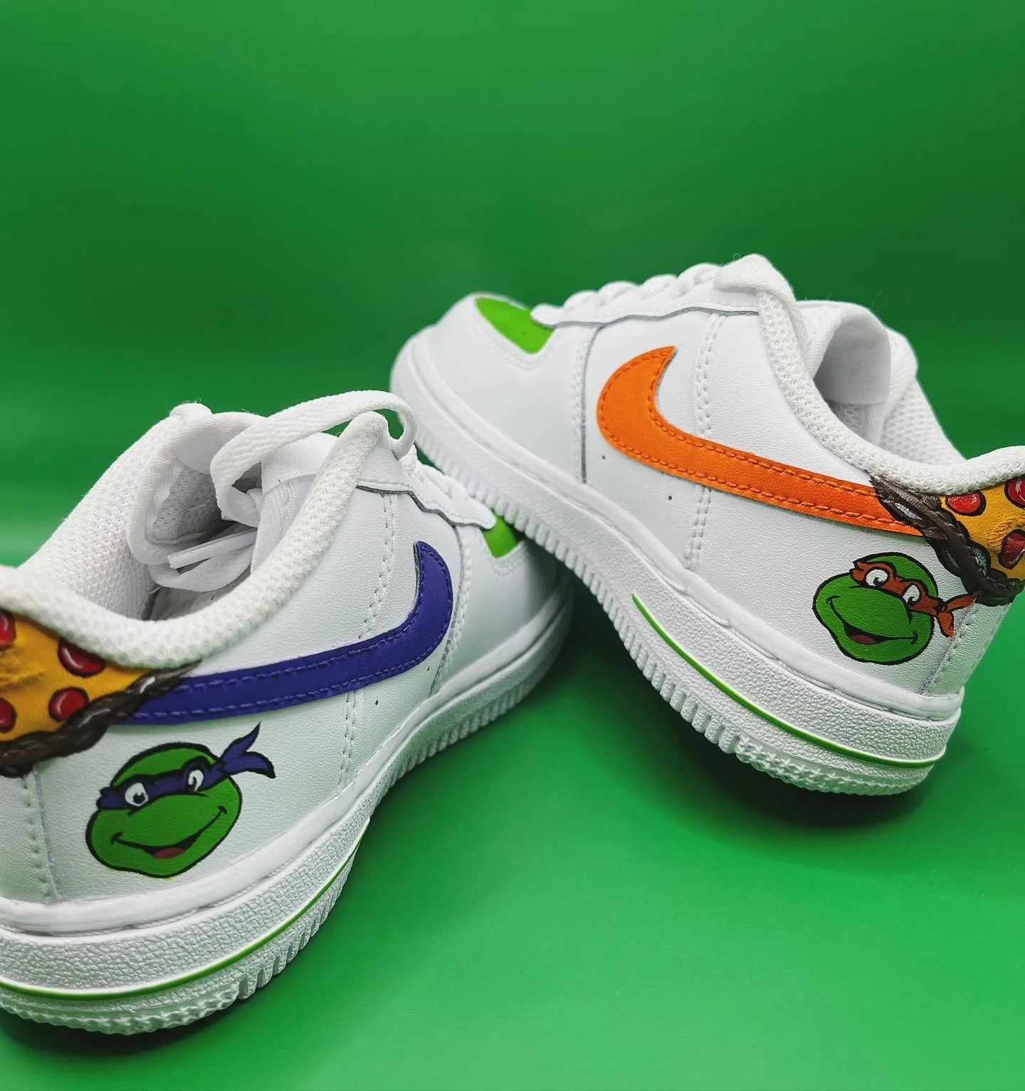 Child's white sneakers featuring Teenage Mutant Ninja Turtles characters, with colorful accents and green, orange, purple, and yellow details on a bright green background.