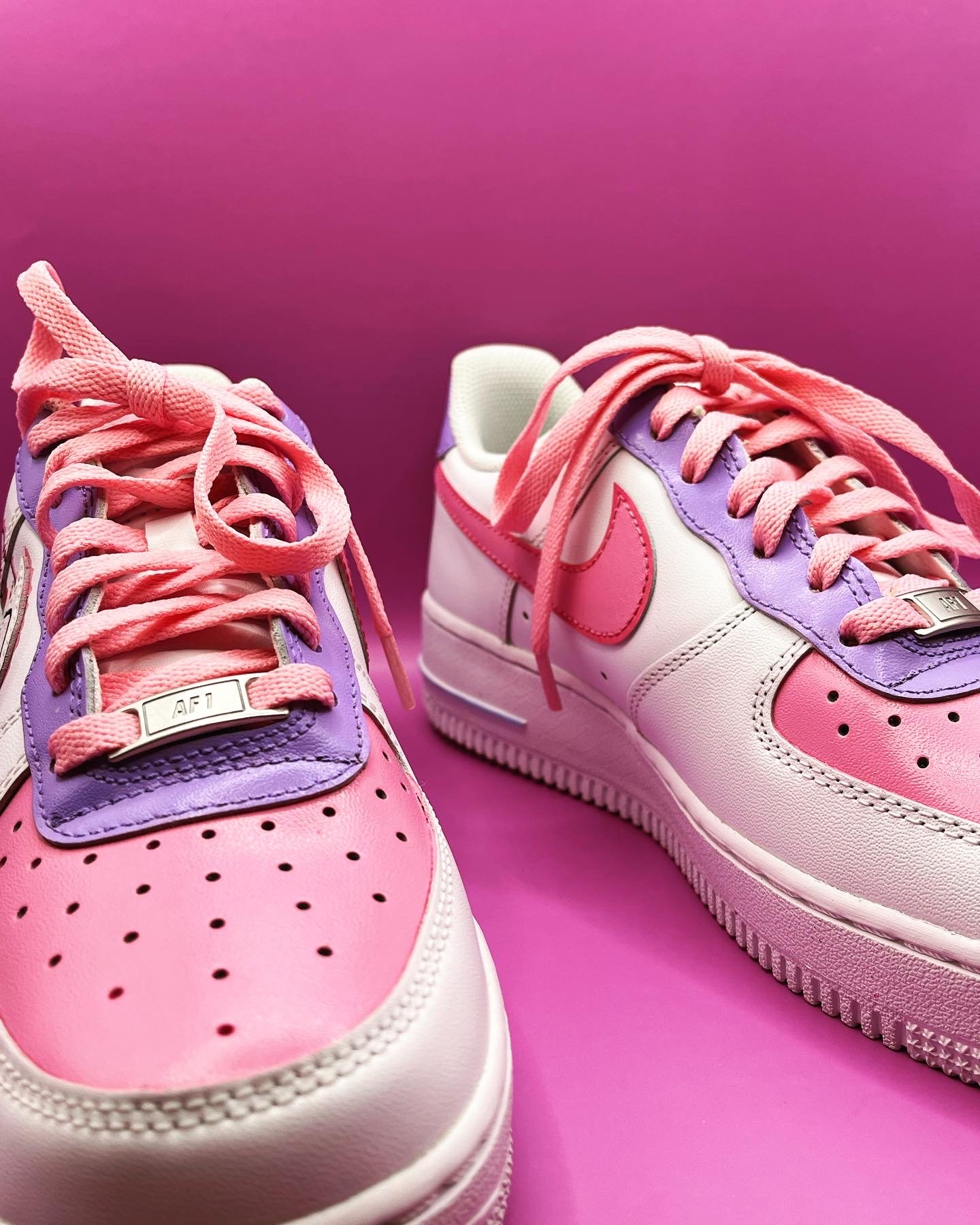 Close-up of pink and purple Nike sneakers with pink laces against a pink background.