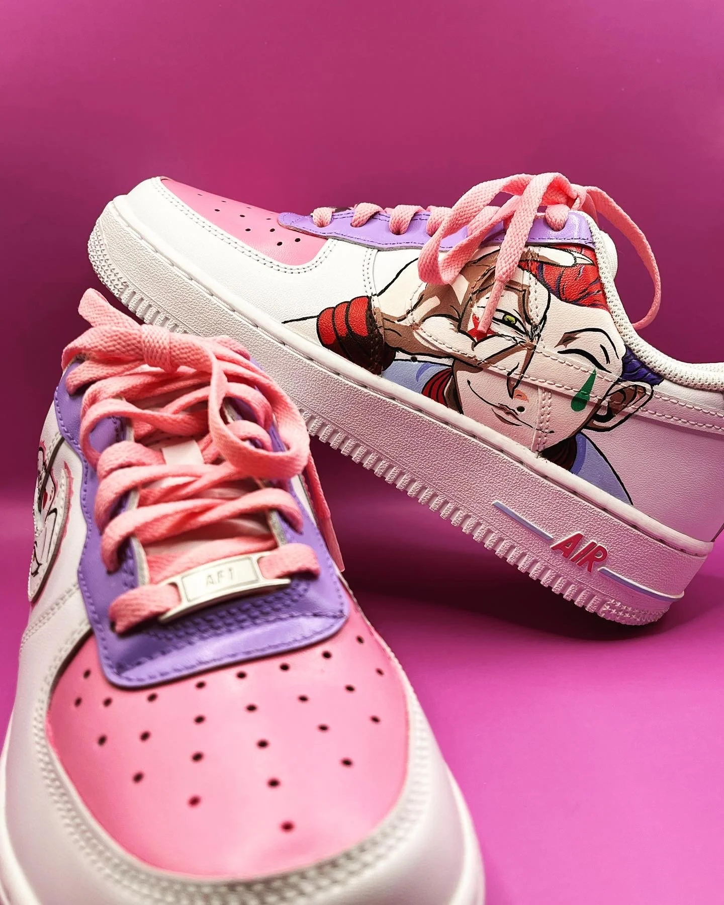 Close-up of a pair of pink, white, and purple Nike Air Force 1 sneakers with cartoon artwork on the sides, pink laces, and a pink background.