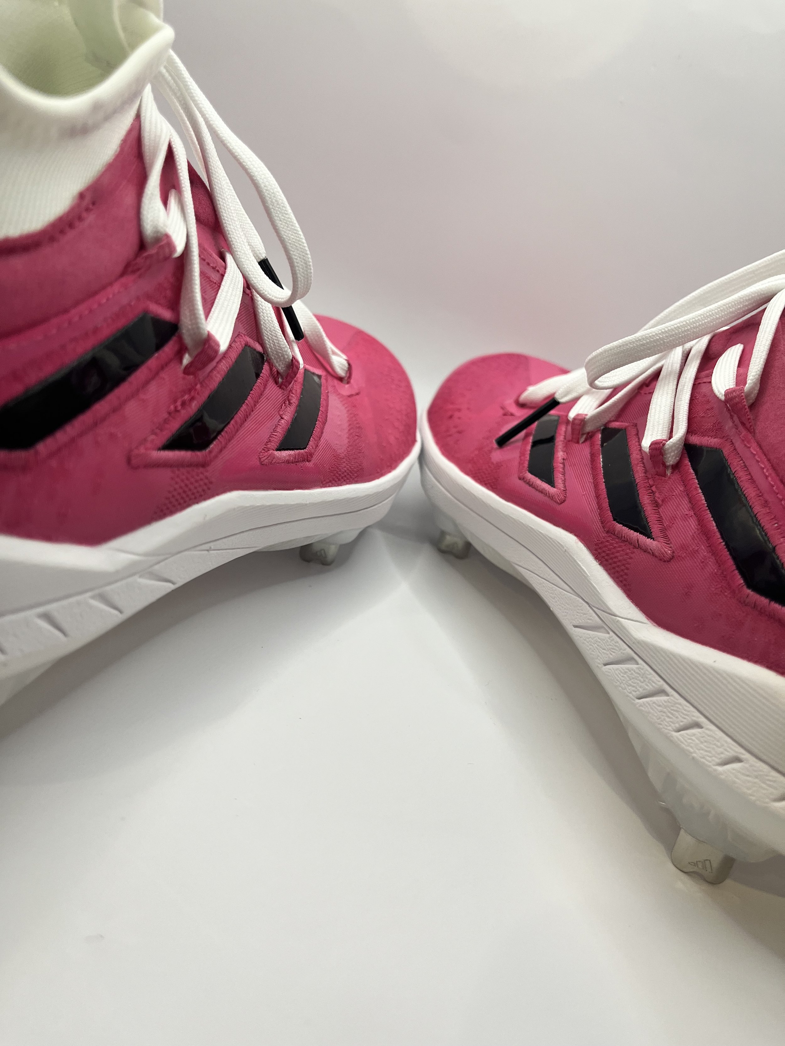 Close-up of pink athletic shoes with white laces and black accents, viewed from the front, placed on a white surface against a white background.