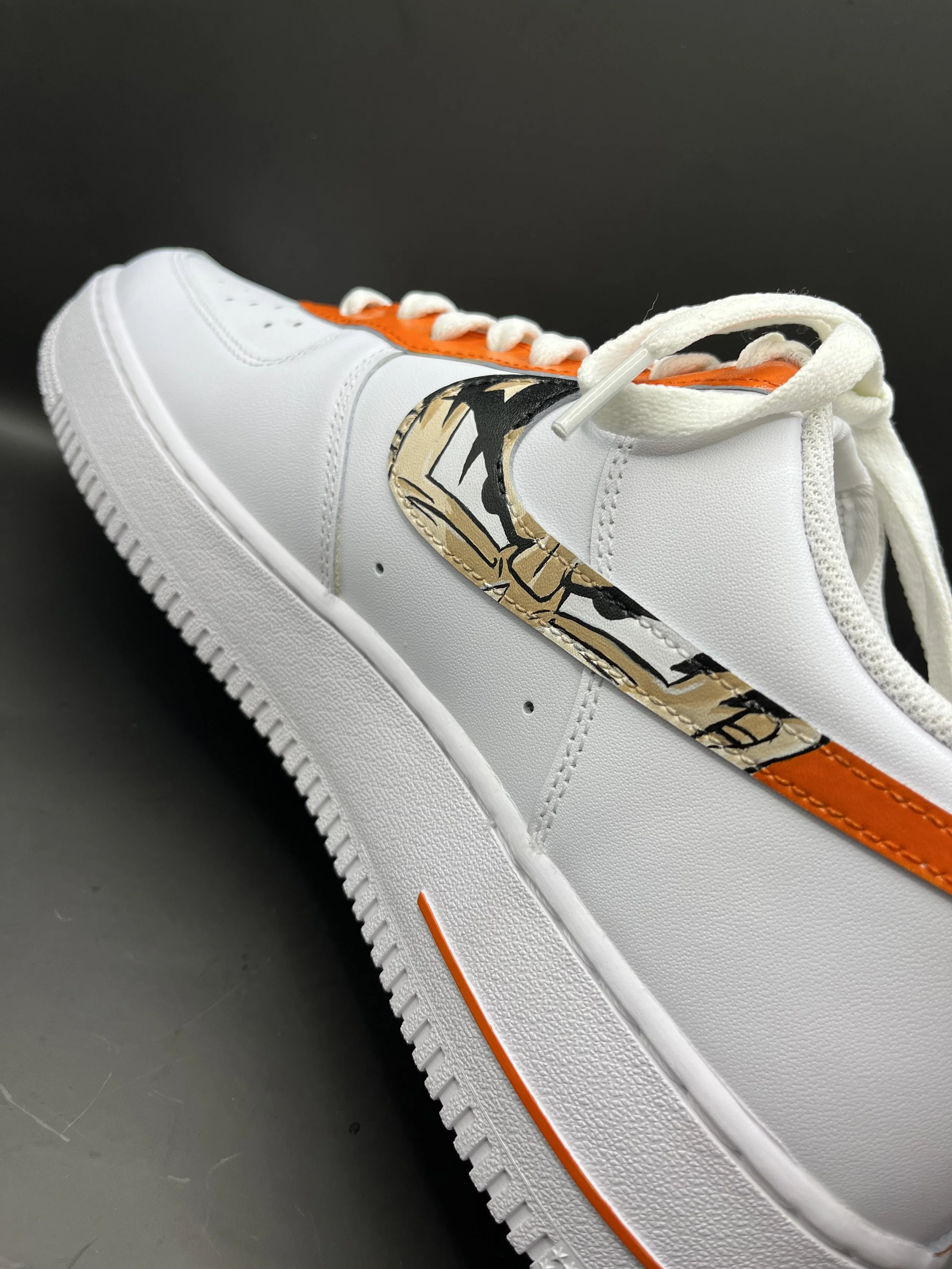 Close-up of a white sneaker with orange accents and a unique gold and black graphic design on the side.