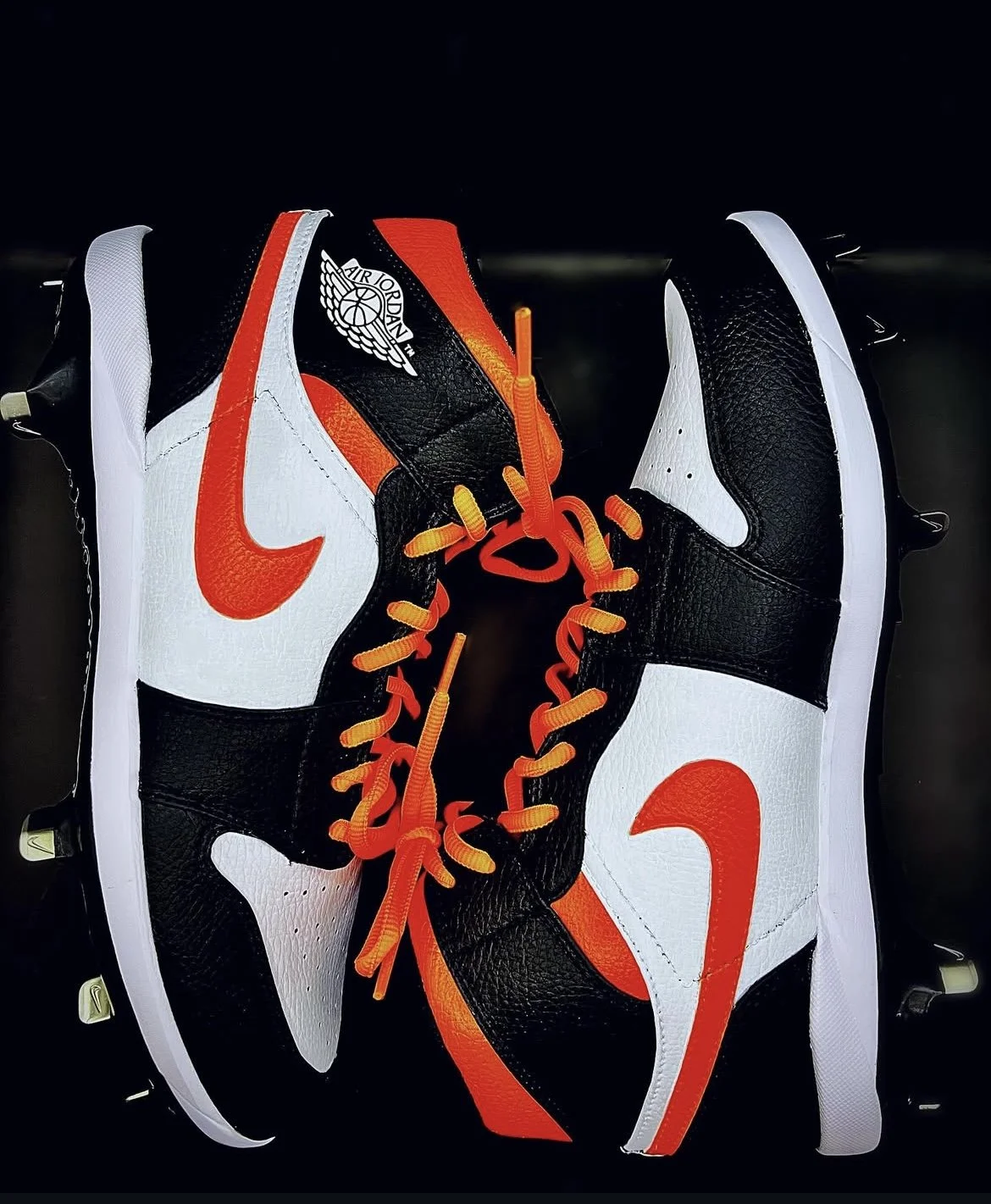 A pair of Nike Air Jordan sneakers, primarily black and white with orange accents and laces, displayed against a black background.