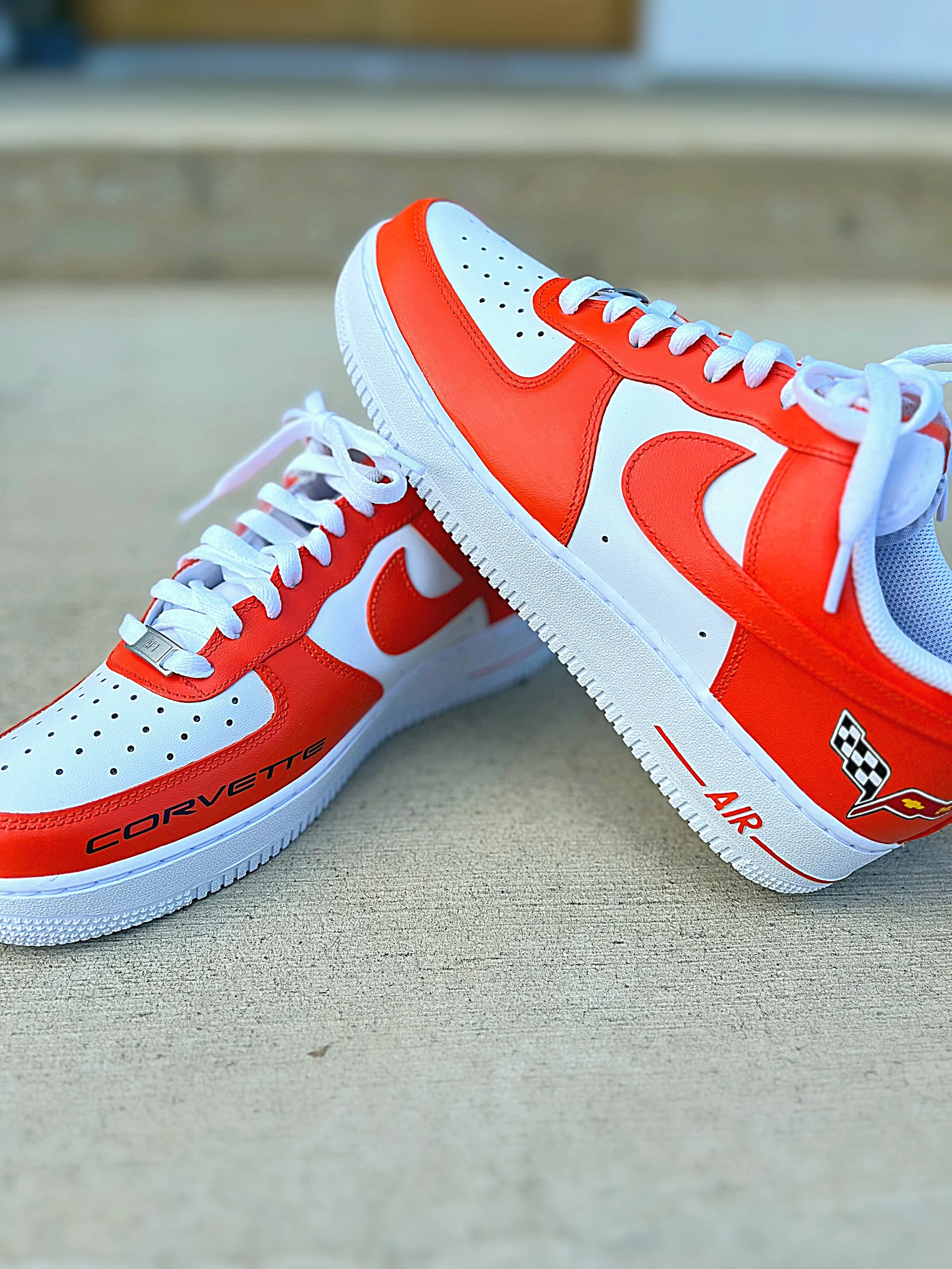 Close-up of a pair of red and white sneakers with racing flags and text on the side, placed on a beige surface.