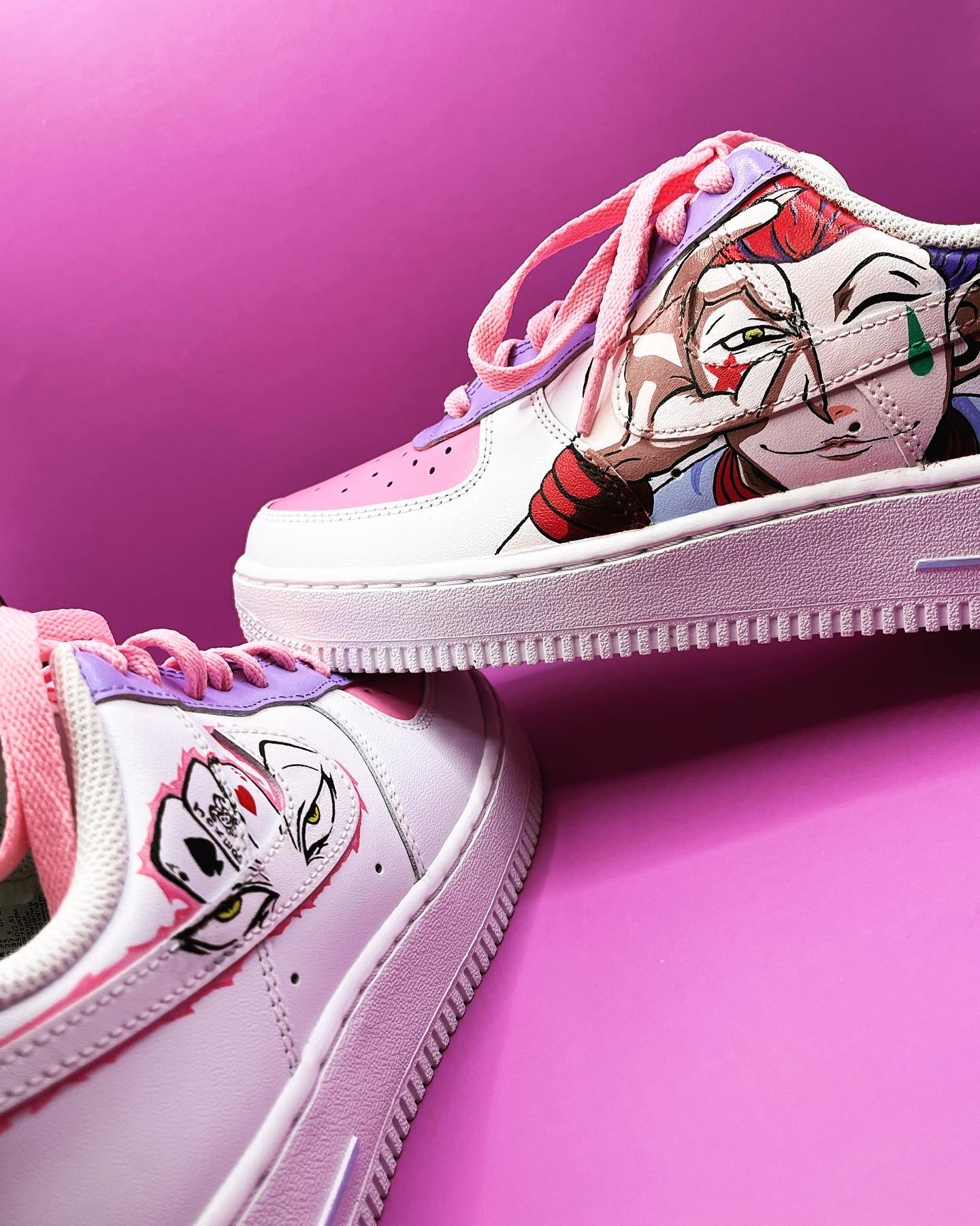 Close-up of a pair of white sneakers with colorful cartoon images of a girl with a skull, pink and purple accents, against a pink background.