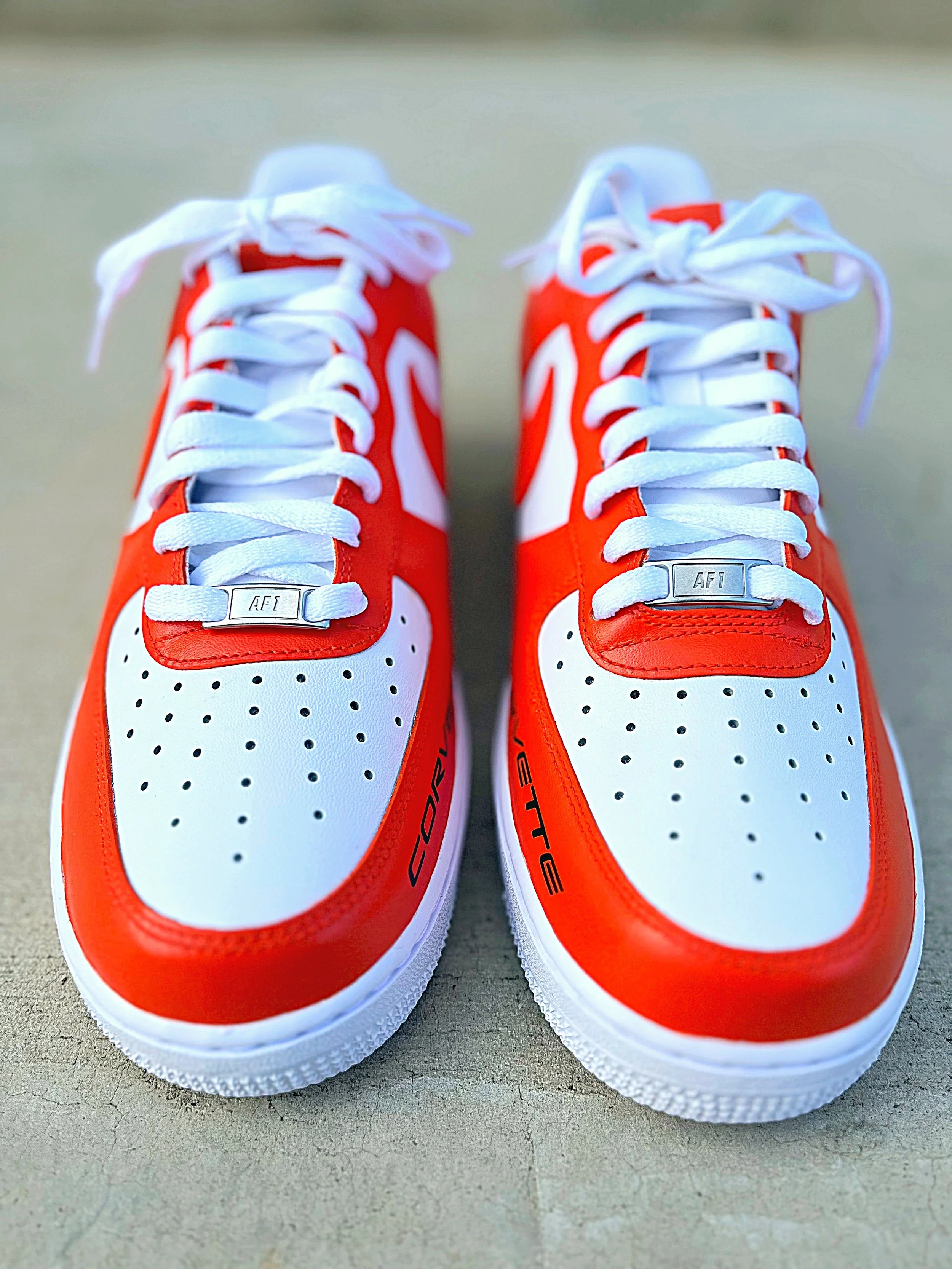 A pair of red and white athletic shoes with white laces placed on a concrete surface.