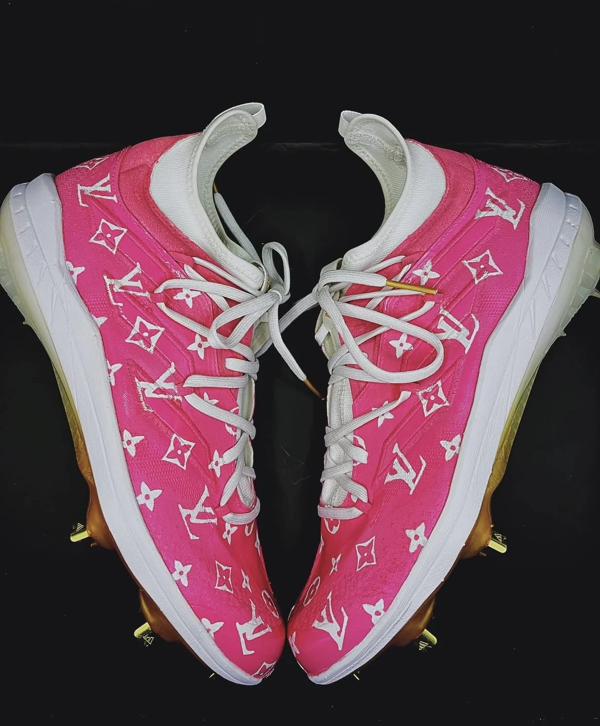 Pink Louis Vuitton sneakers with white logo pattern, white laces, and transparent soles, positioned against a black background.