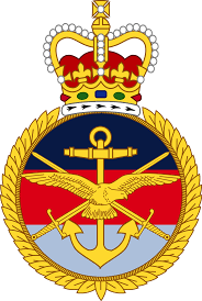 Emblem featuring a crown above a circular badge with an anchor, wings, and swords arranged in a symmetrical design.