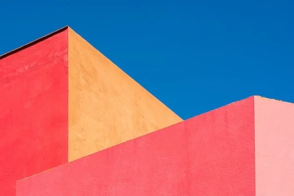 Close-up of colorful modern building with bright red, yellow, and pink sections against a clear blue sky.