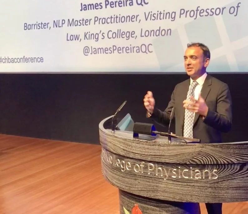 A man in a suit speaking at a podium with the words 'Royal College of Physicians' engraved on it, in a conference room. A projected slide behind him shows his name, James Pereira QC, along with his titles and affiliation, and a Twitter handle '@James