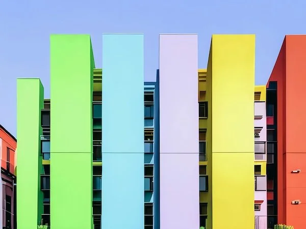 Colorful modern apartment building with vertically aligned panels in shades of green, blue, pink, yellow, and orange, against a clear blue sky.