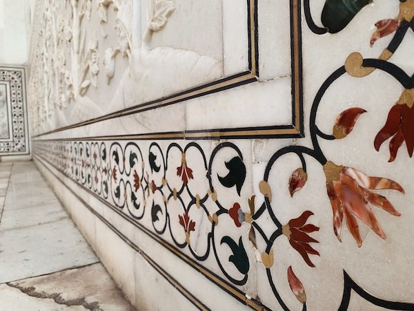 Close-up of ornate marble wall with decorative black, red, and cream inlaid patterns including flowers and geometric designs.