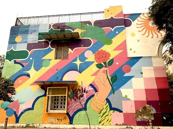 Colorful mural on building wall featuring abstract shapes and a large hand holding a red rose.