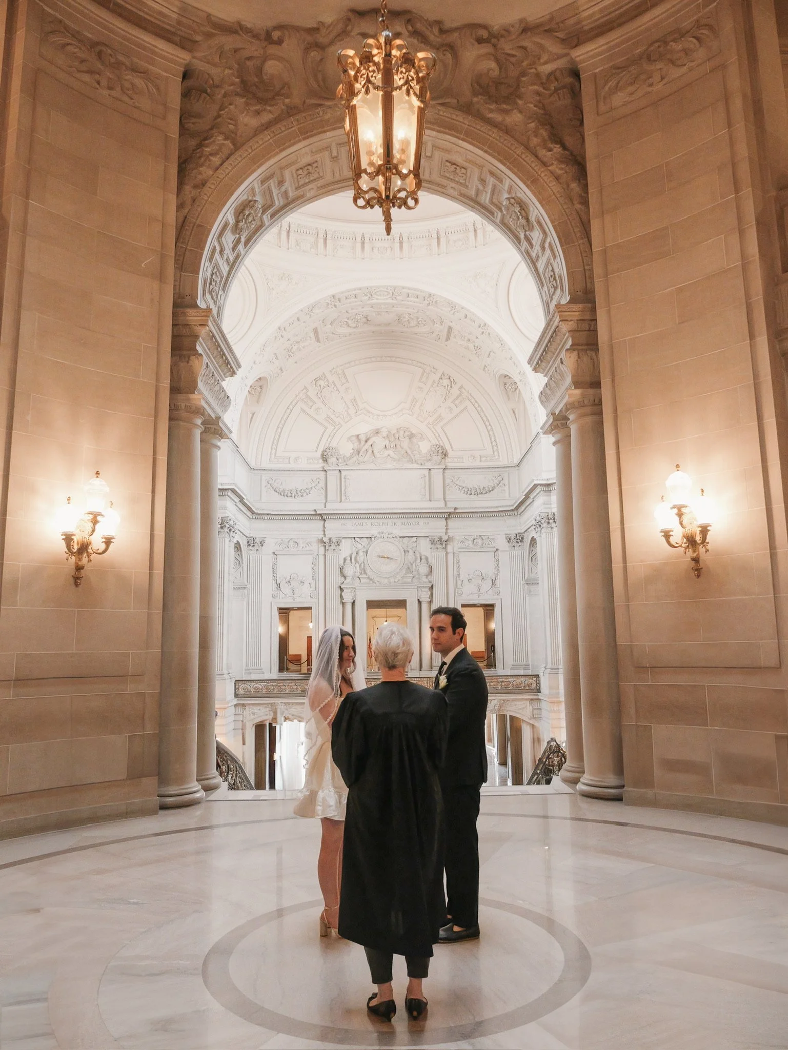 A bride and groom standing in San Francisco with their officiant under an ornate lantern.