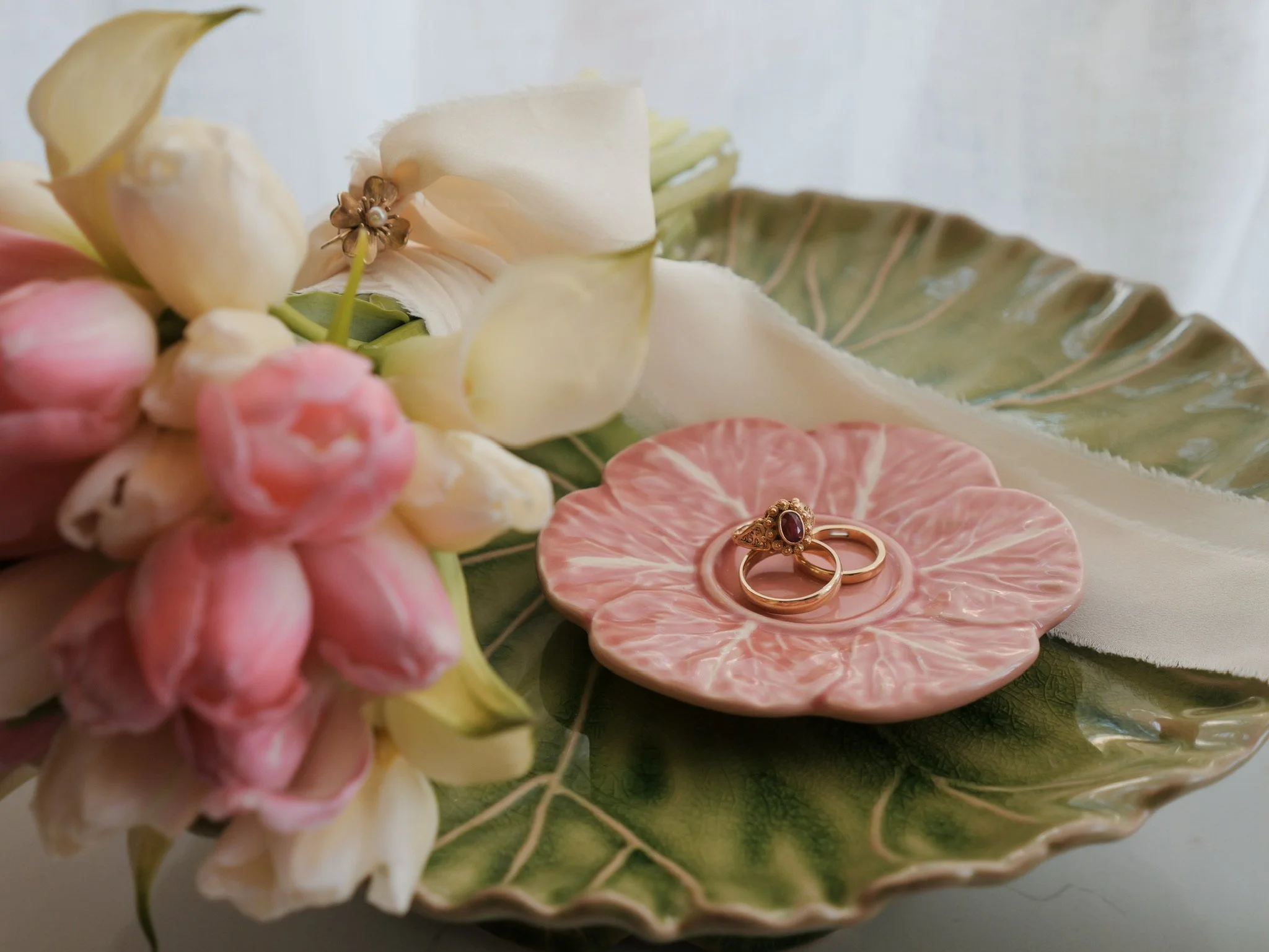 Close-up of a floral arrangement with pale pink, white, and cream flowers, green leaves, and two gold rings with a red gemstone, placed on a decorative plate.