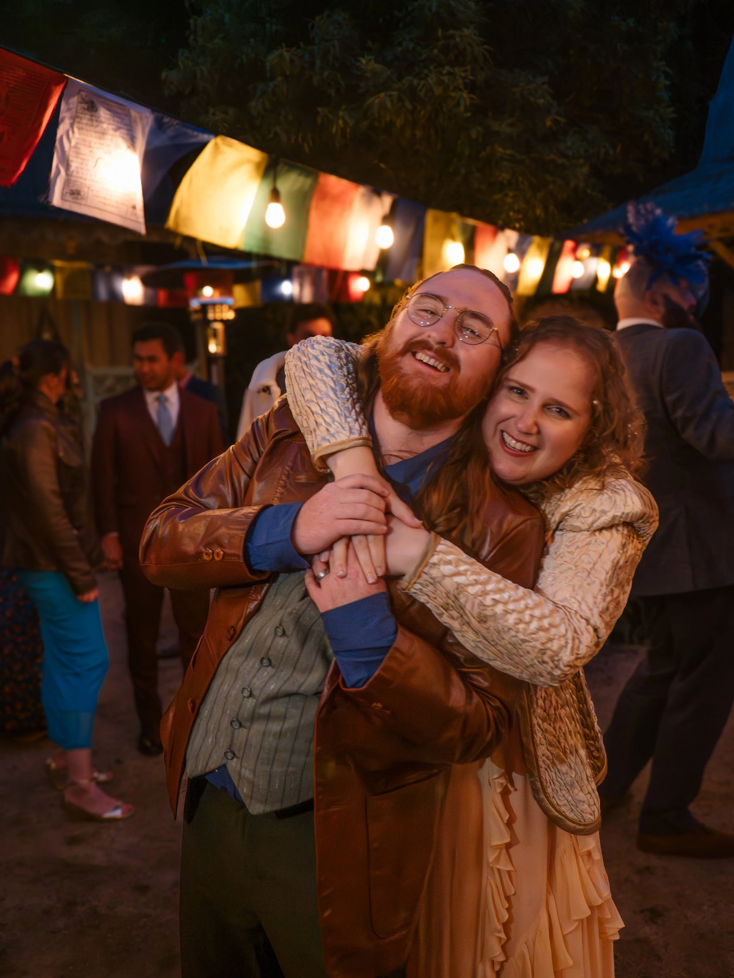 Happy couple dancing at a celebration under colorful flags and string lights at night.