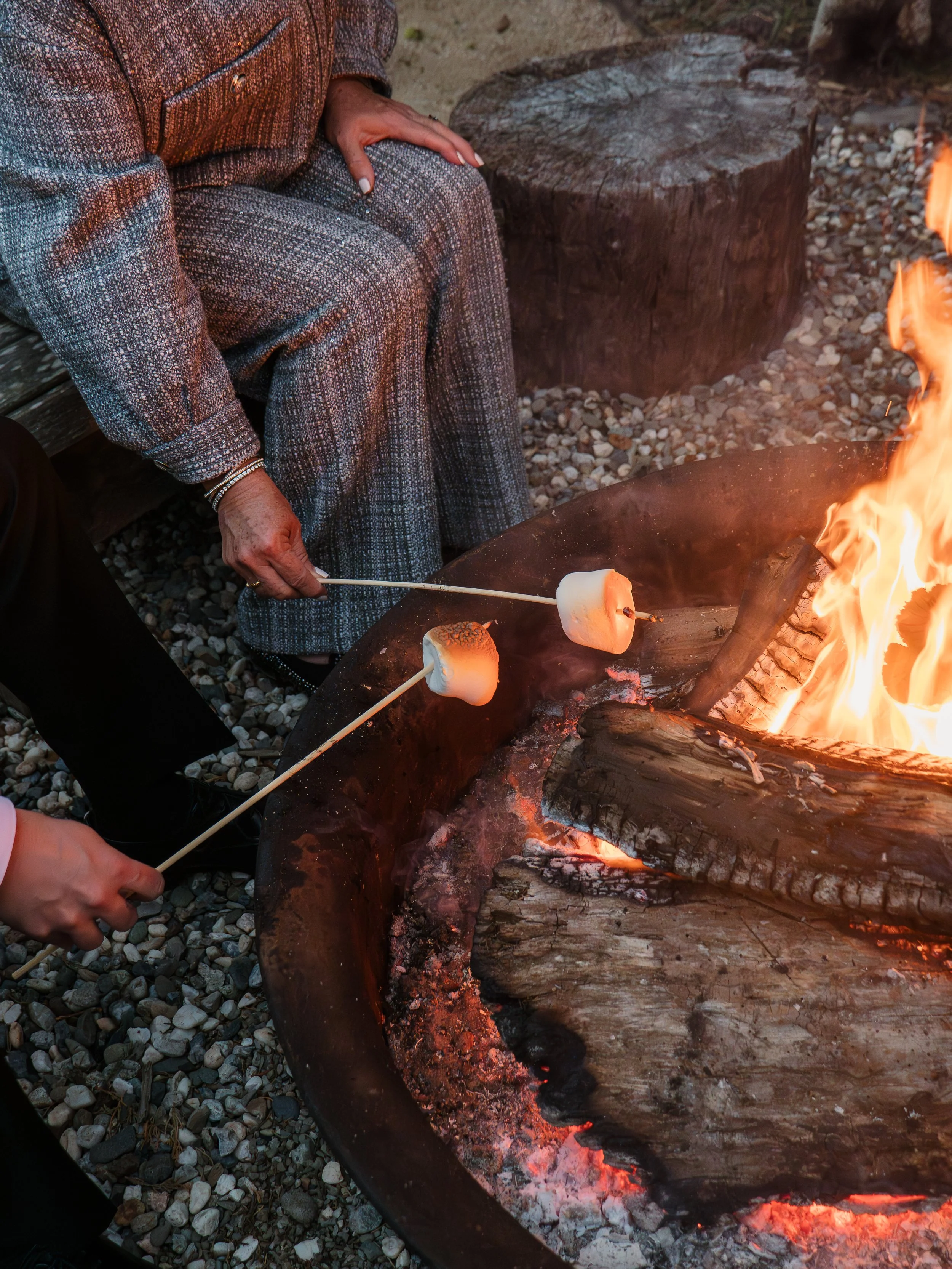 Someone roasting marshmallows over an open campfire with logs and rocks surrounding it.