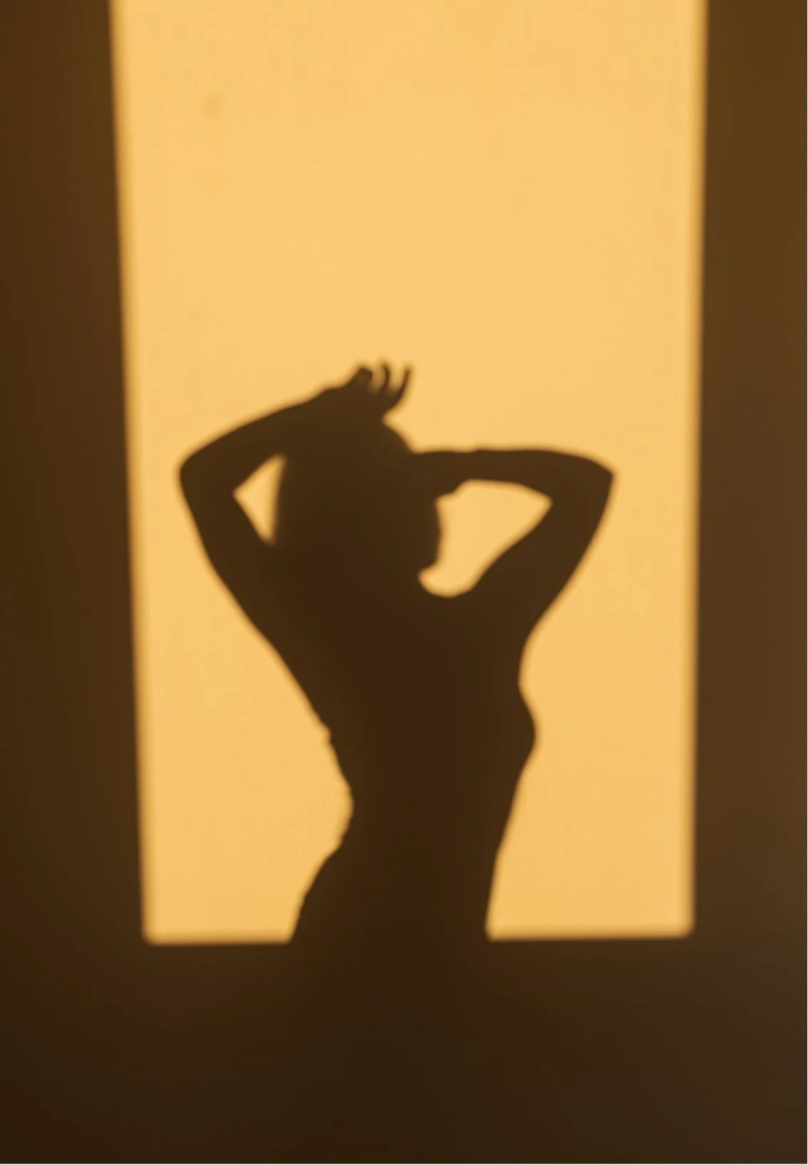 Shadow of a woman with hands in her hair, projected onto a yellow background.